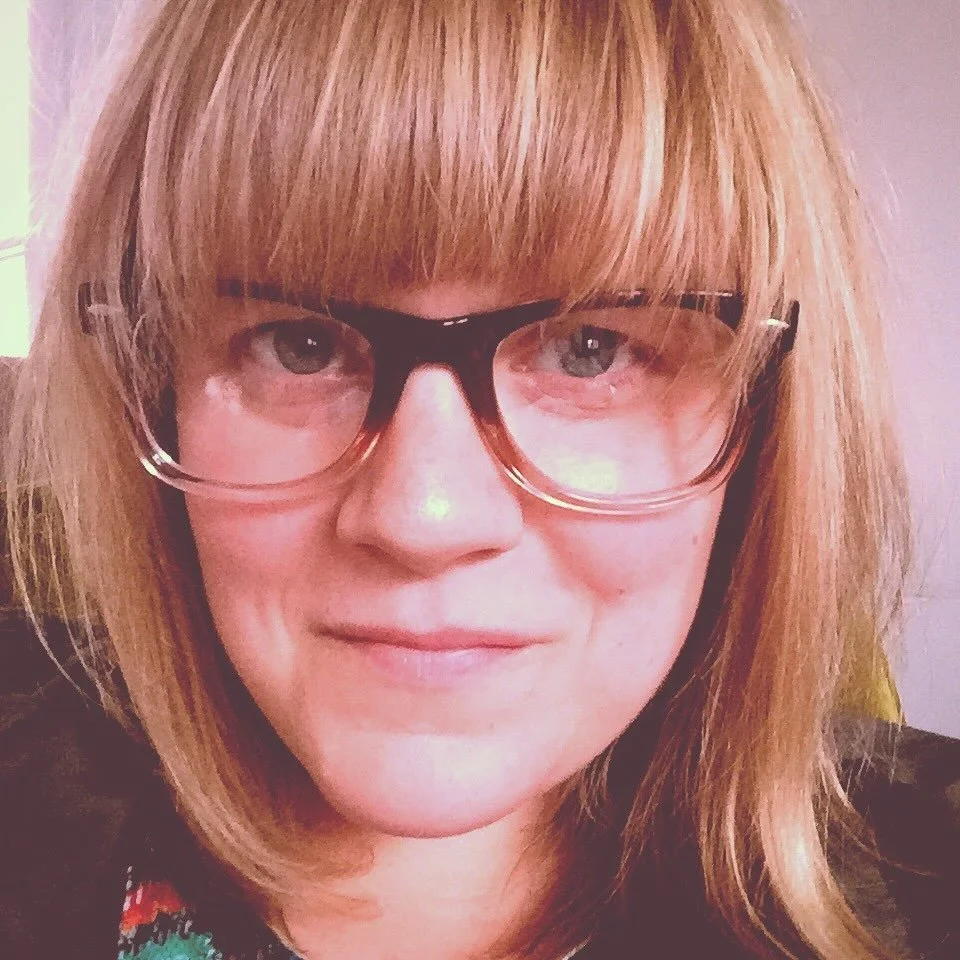 Close-up of a woman with blonde hair and glasses, smiling.