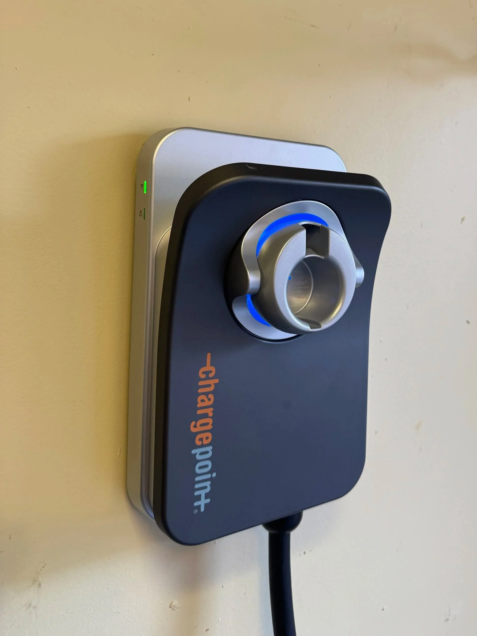 ChargePoint electric vehicle charging station mounted on a beige wall, with a black charging cable hanging from it.