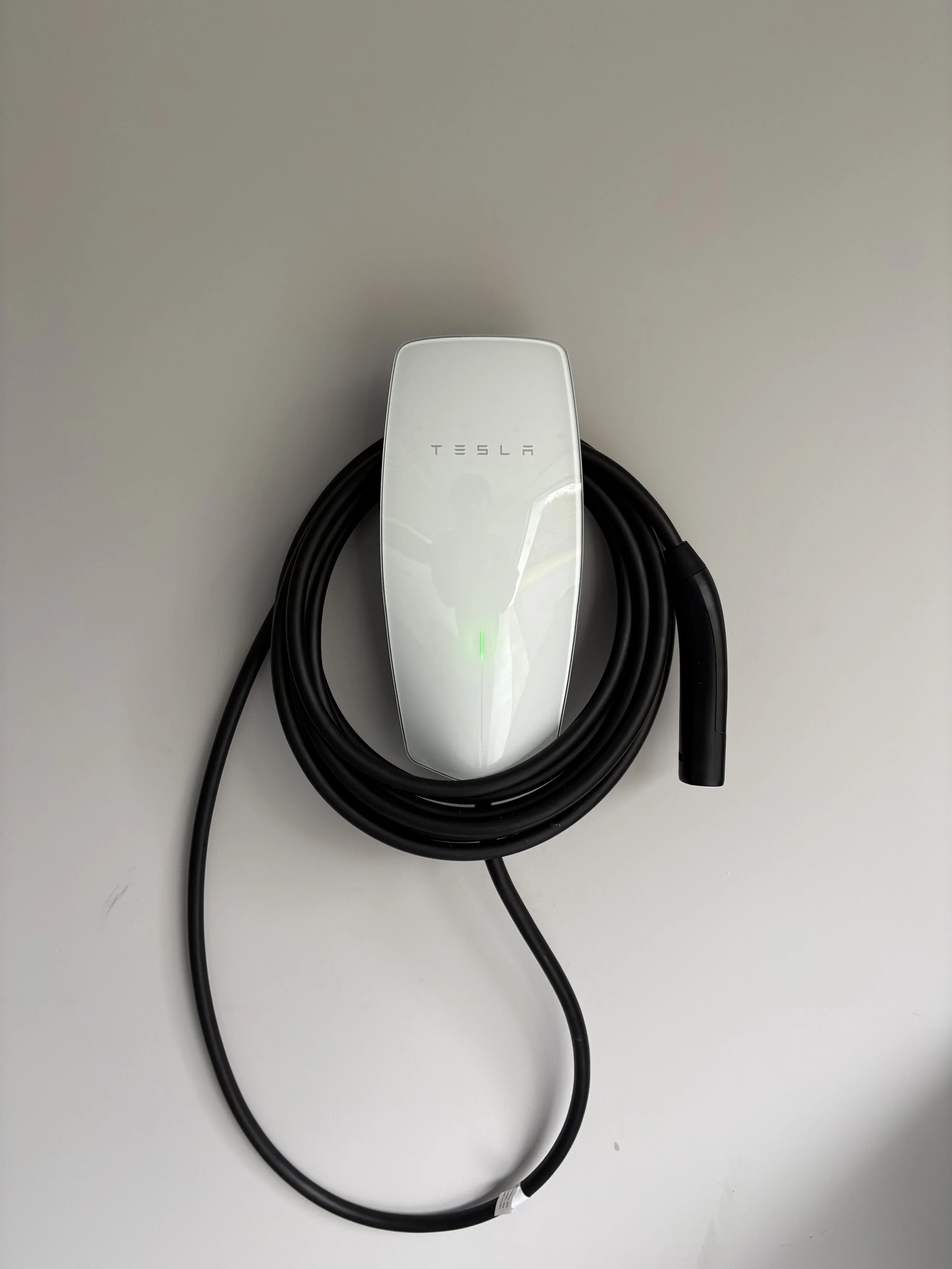 Tesla electric vehicle charging station with a connected black charging cable on a light-colored surface.