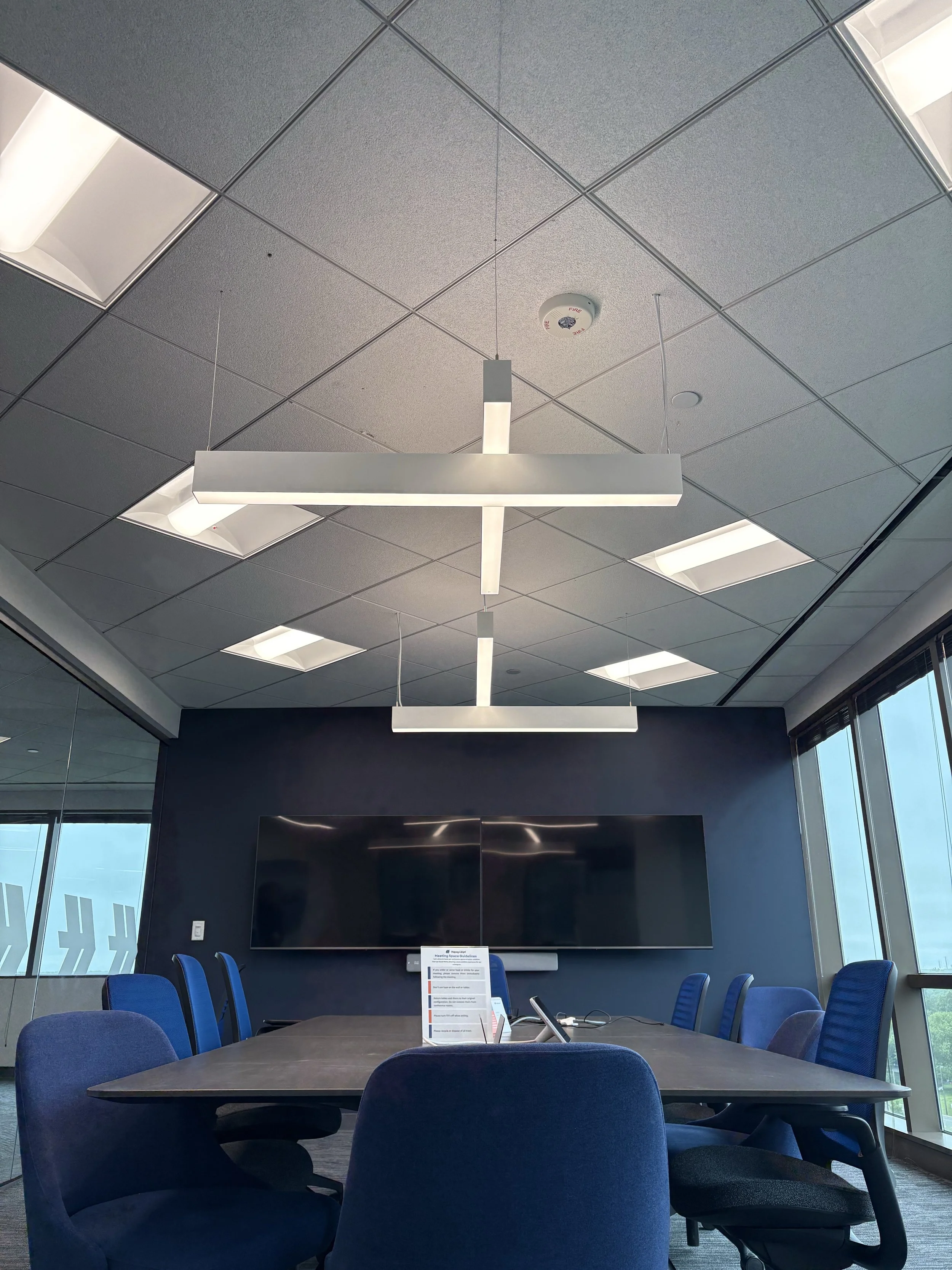 Empty modern conference room with a long table, blue chairs, large wall-mounted television, and large windows with views outside.