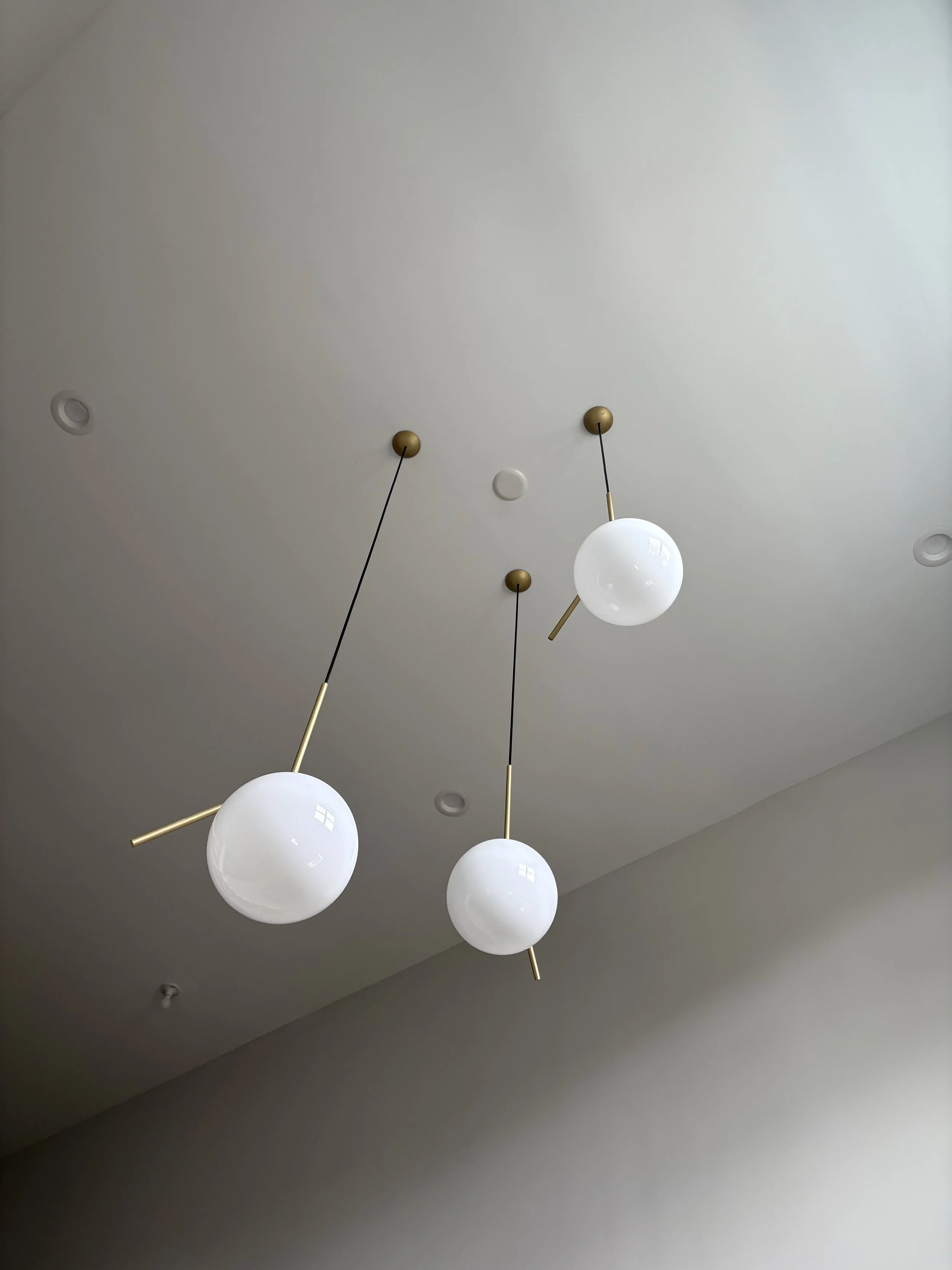 Modern ceiling pendant lights with white glass globes and gold accents against a white ceiling.