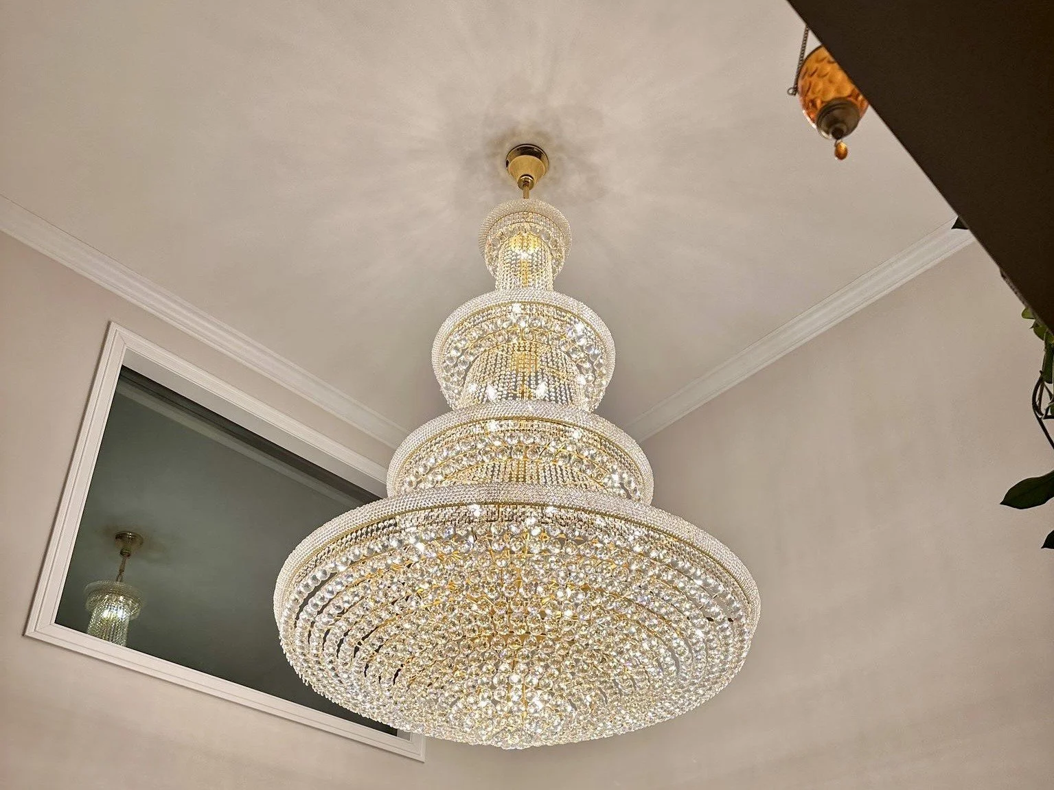 Large, ornate crystal chandelier hanging from ceiling in a room with a mirror and crown molding.