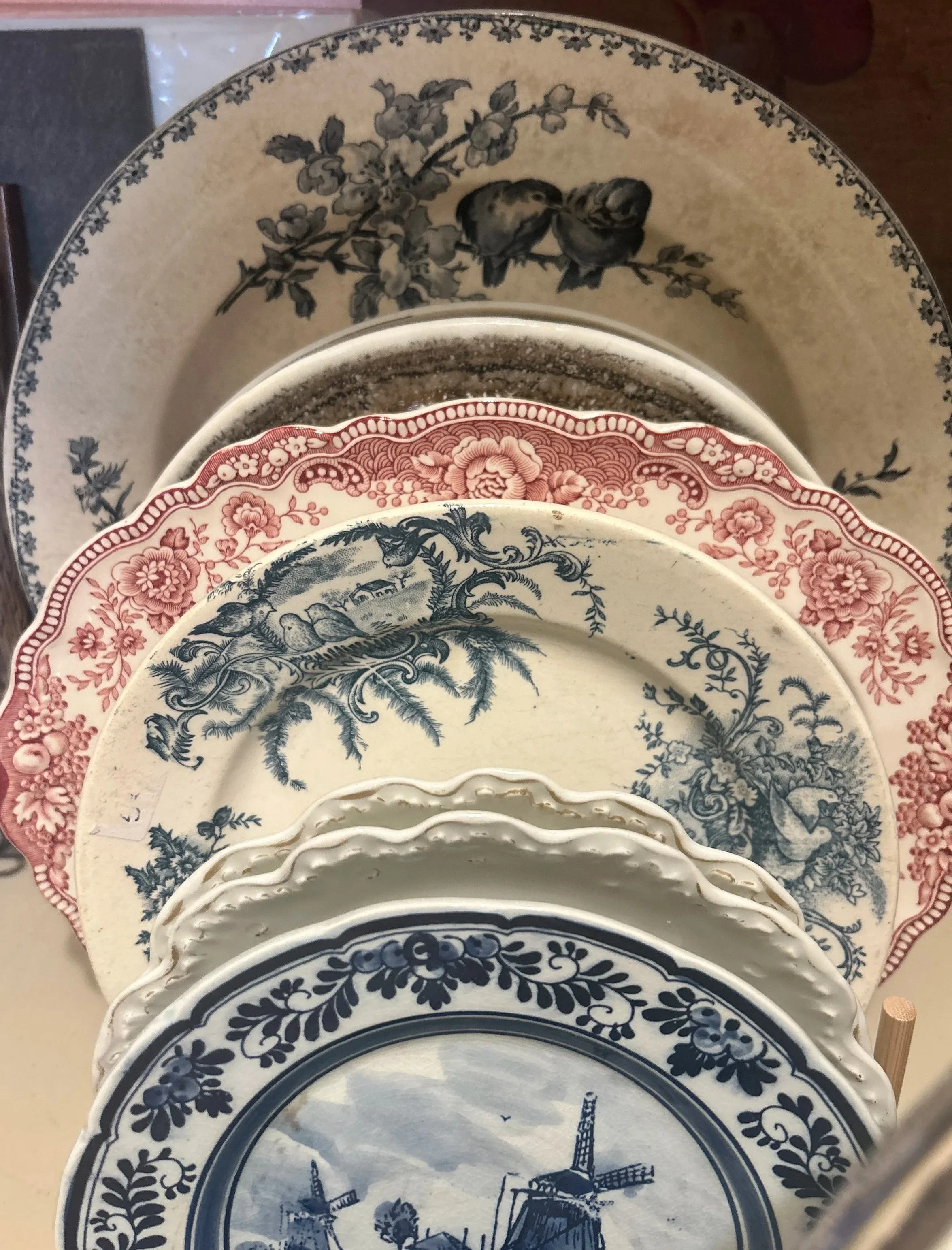 A collection of decorative plates with floral and windmill designs, stacked on top of each other, in various colors including blue, pink, and beige.