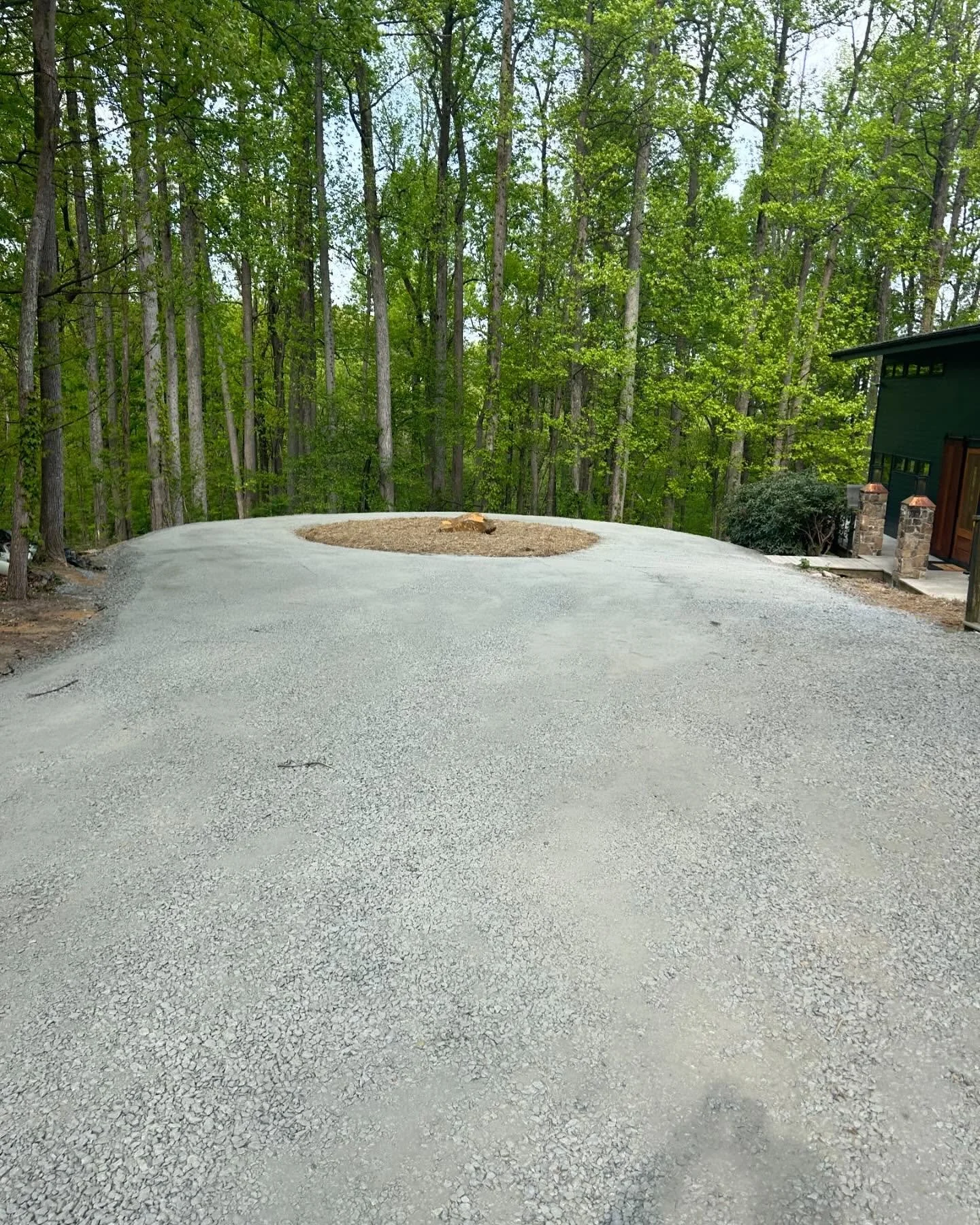 Gravel driveway at a house with a wooded background and a green house on the right side.