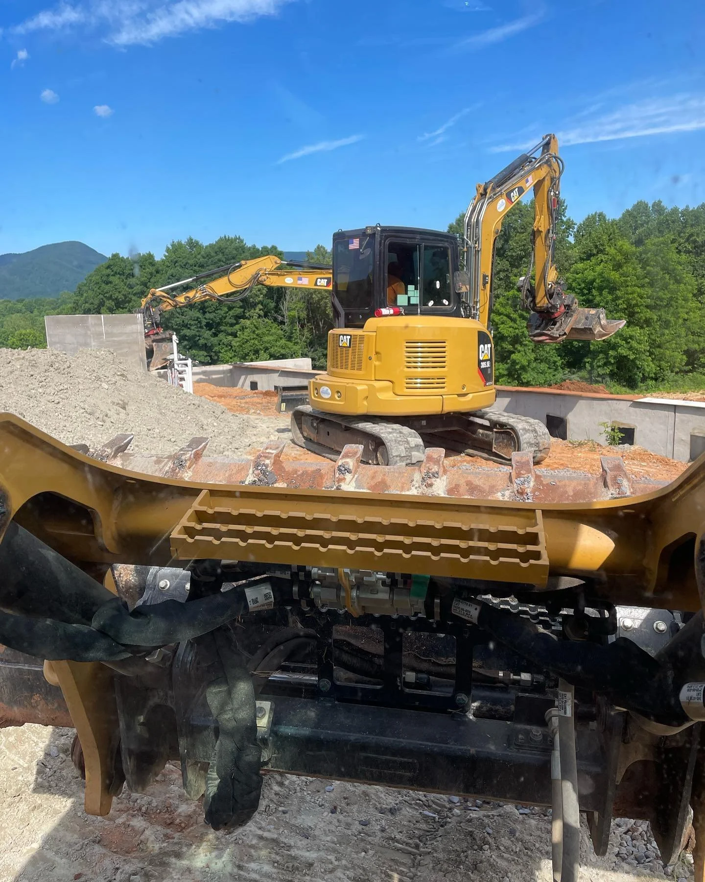 A bulldozer operating on a construction site with mountains in the background, viewed through a vehicle's windshield.