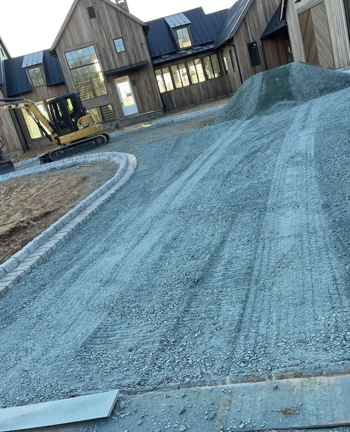 Construction site with a small excavator and a mound of gravel in front of modern wooden houses.
