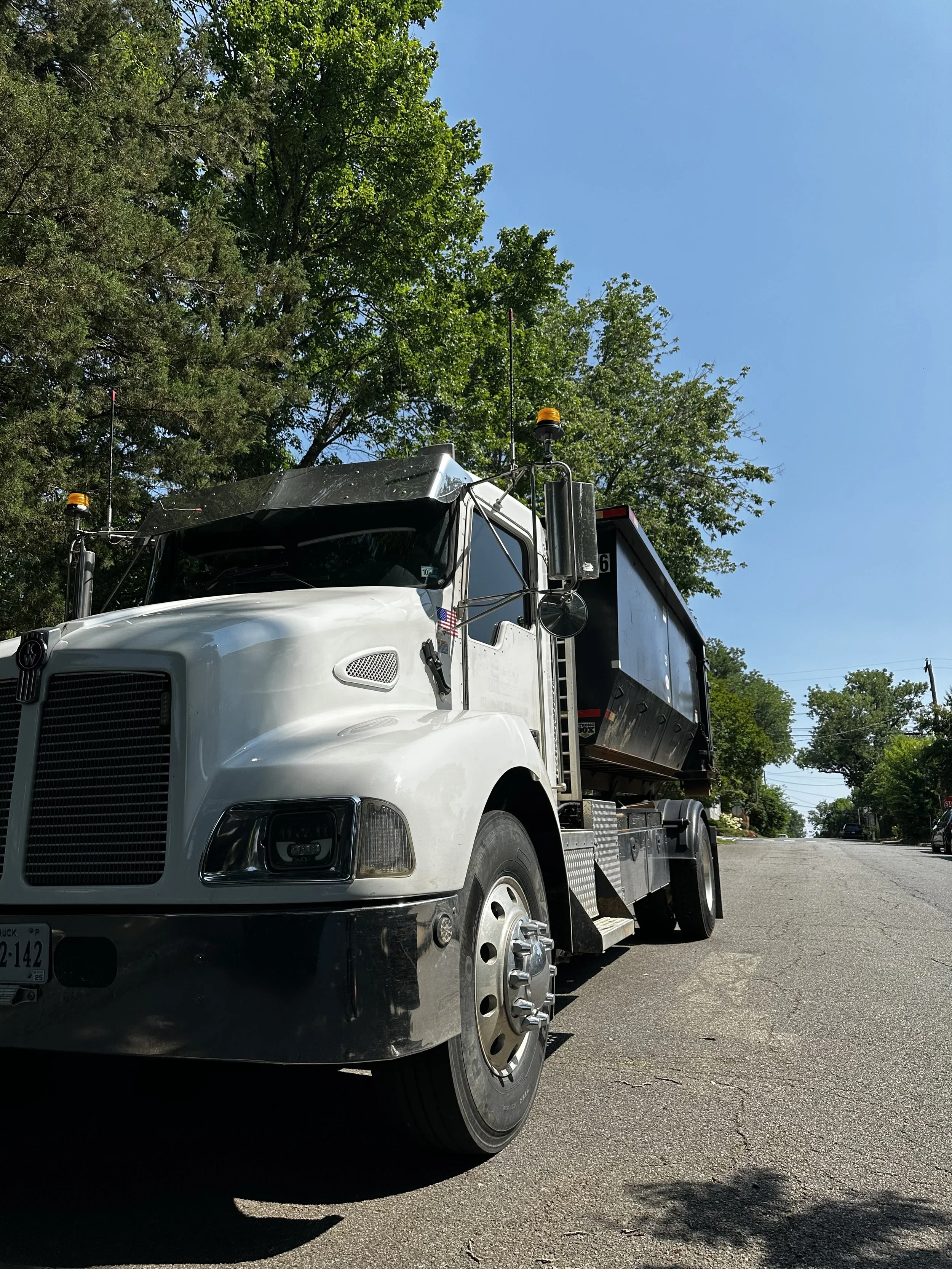 A white utility truck parked on a street with trees and a clear blue sky in the background.
