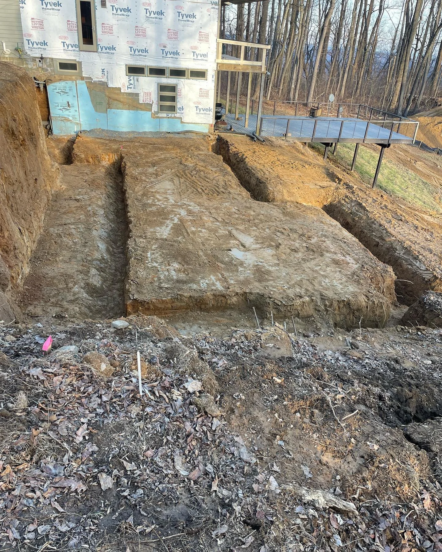Erosion or excavation site in front of a house under construction with exposed soil and trenches.
