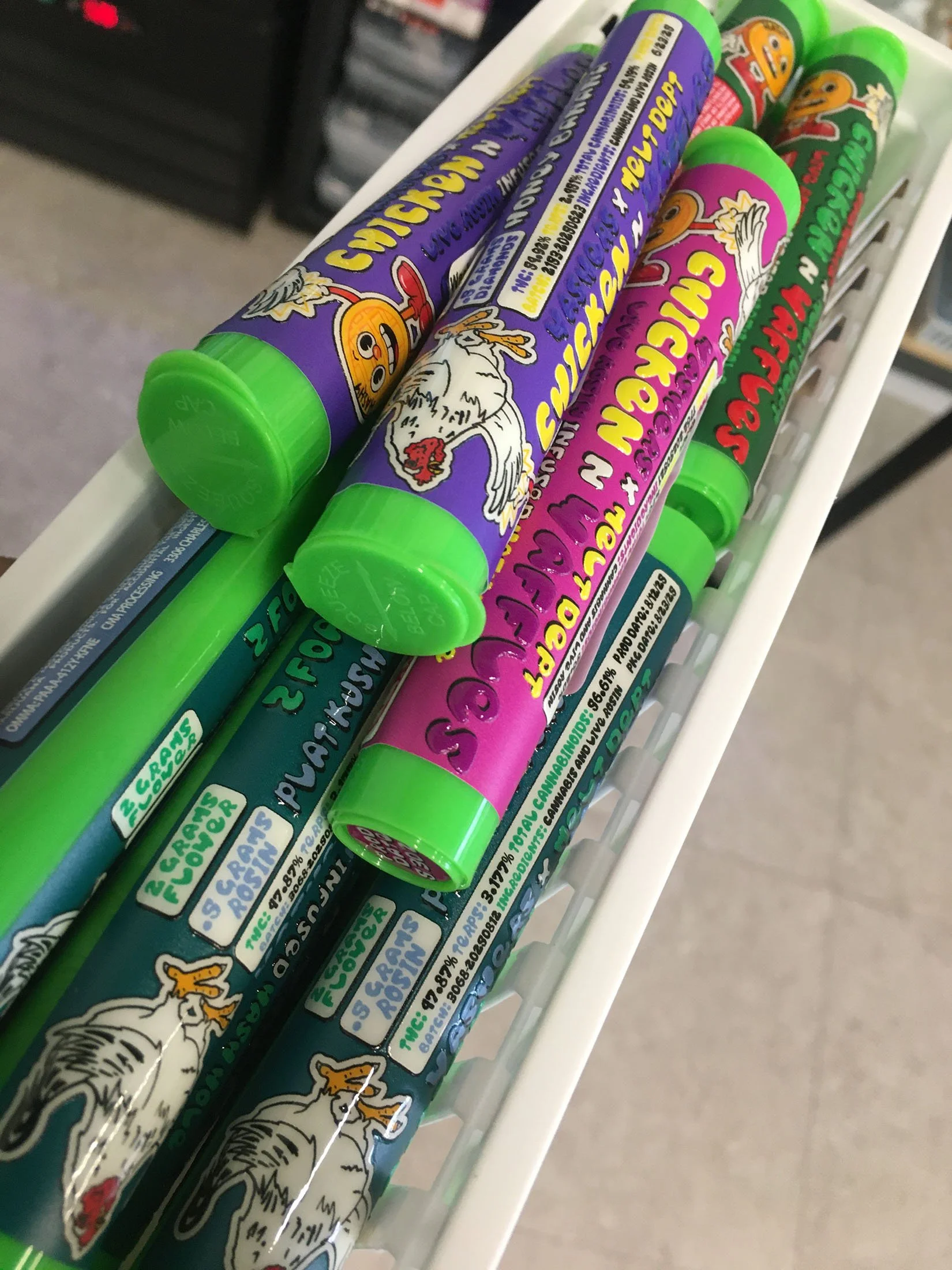 Colorful tubes of Chickenscratch brand crop spray in green, purple, and pink, with chicken illustrations and cartoon characters on a store shelf.