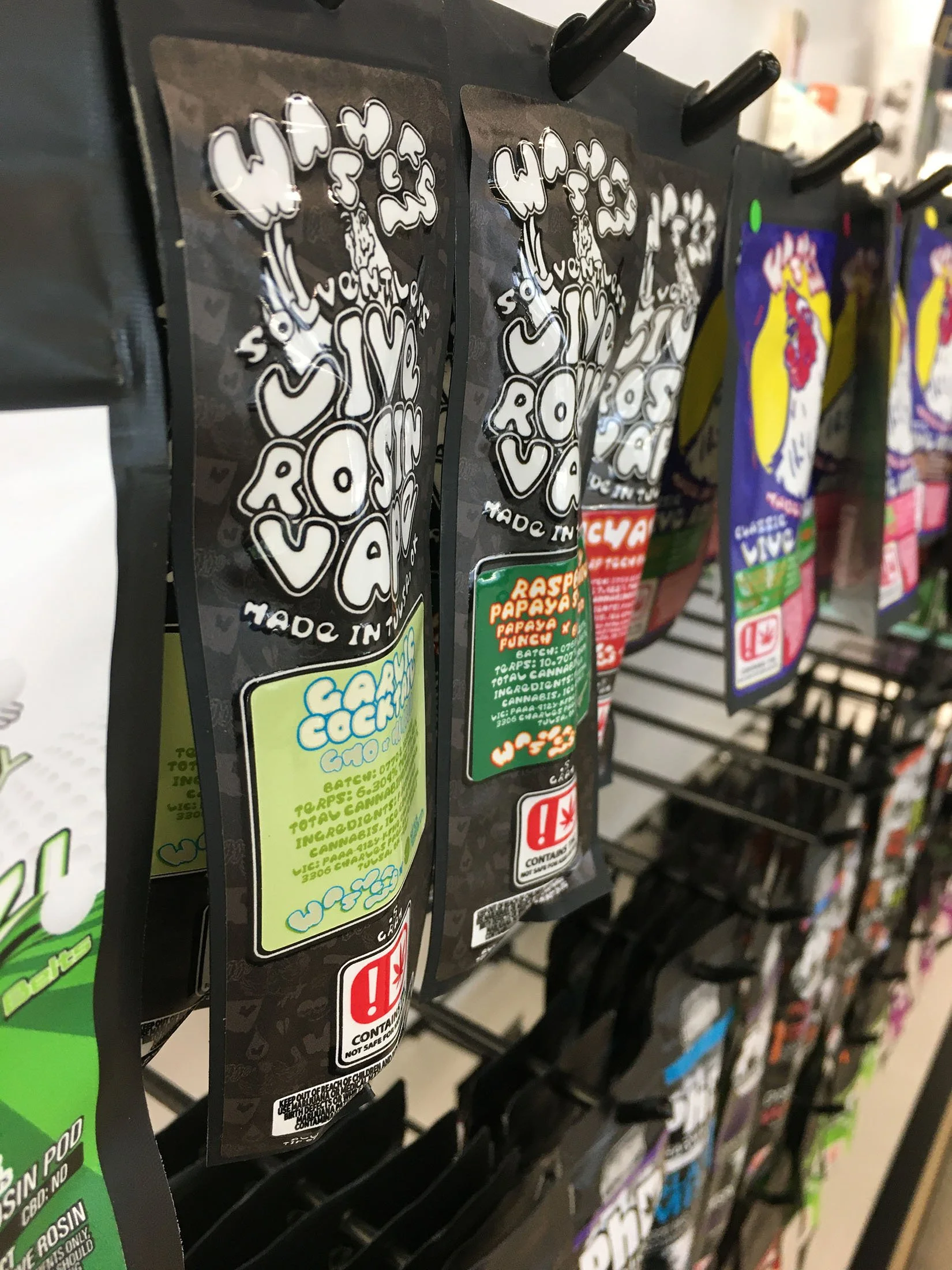 Assorted cannabis concentrate packaging hanging on a store display rack, with colorful labels and branding.