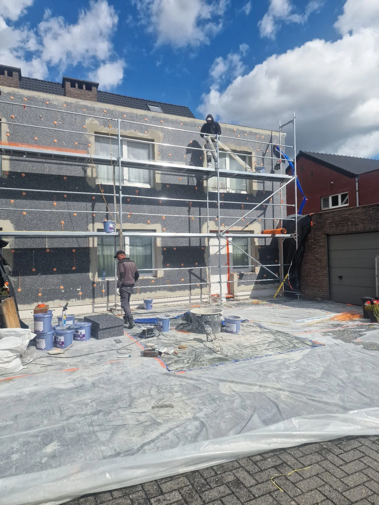 Construction workers and scaffolding on a house exterior during renovation under a partly cloudy sky.
