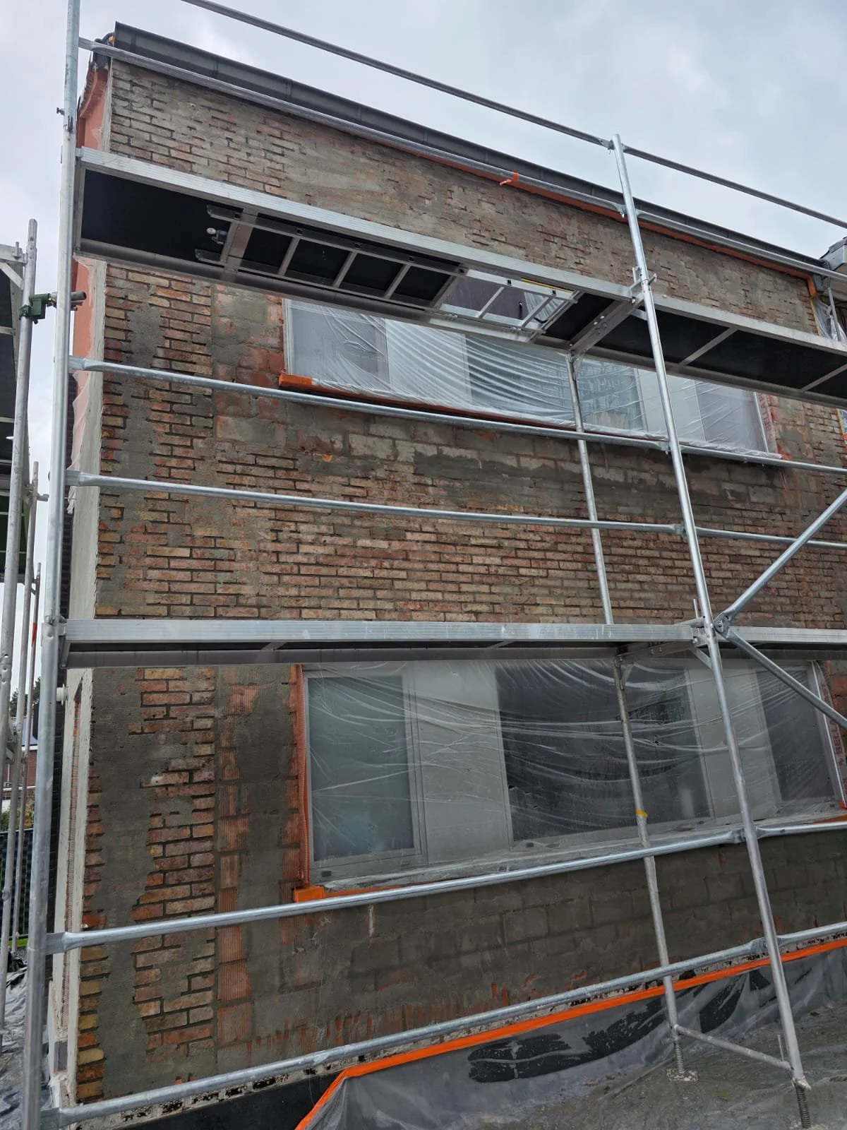 Building under construction with brick wall, scaffolding, and plastic-covered windows.