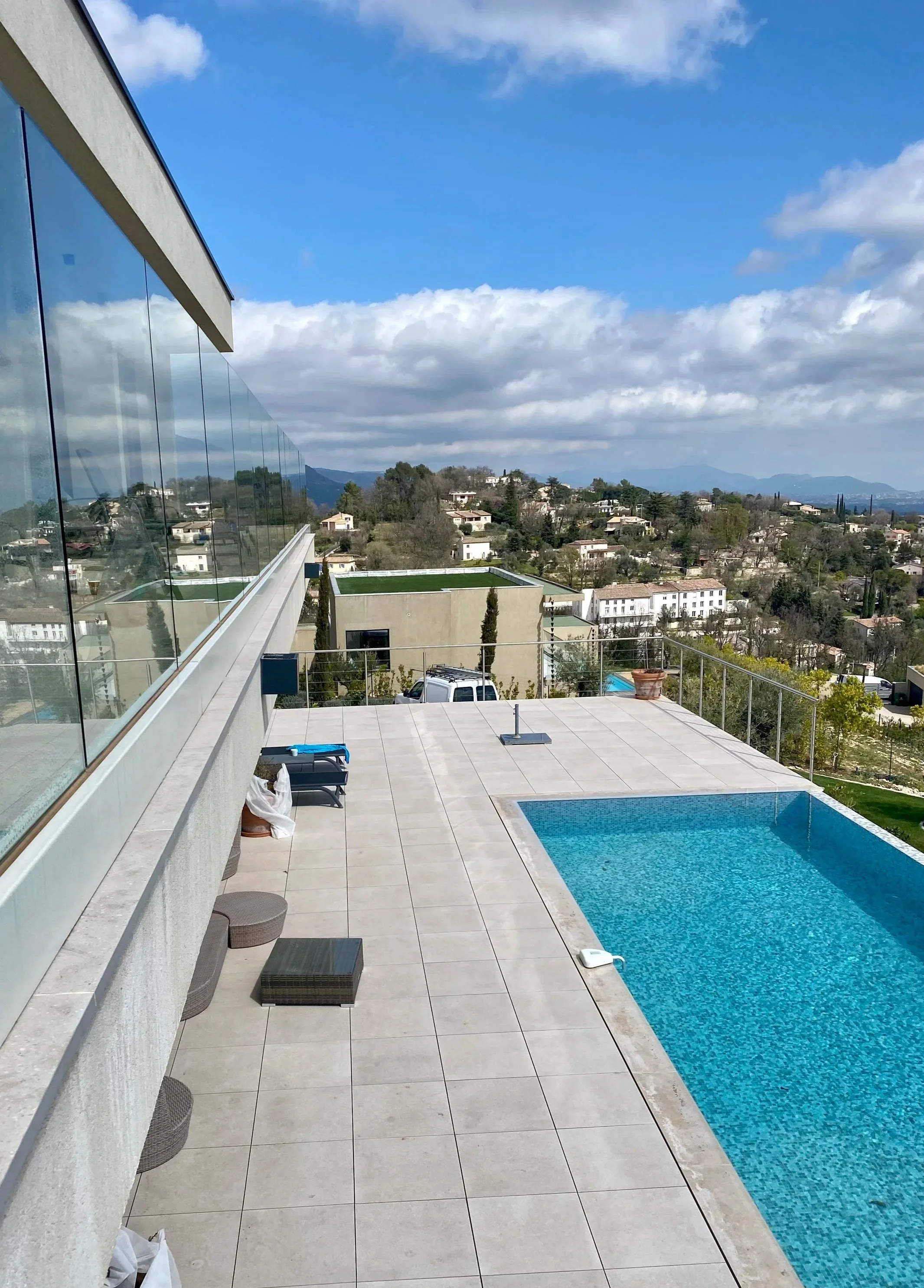 Rooftop swimming pool with view of residential neighborhood and mountains in the distance under partly cloudy skies.