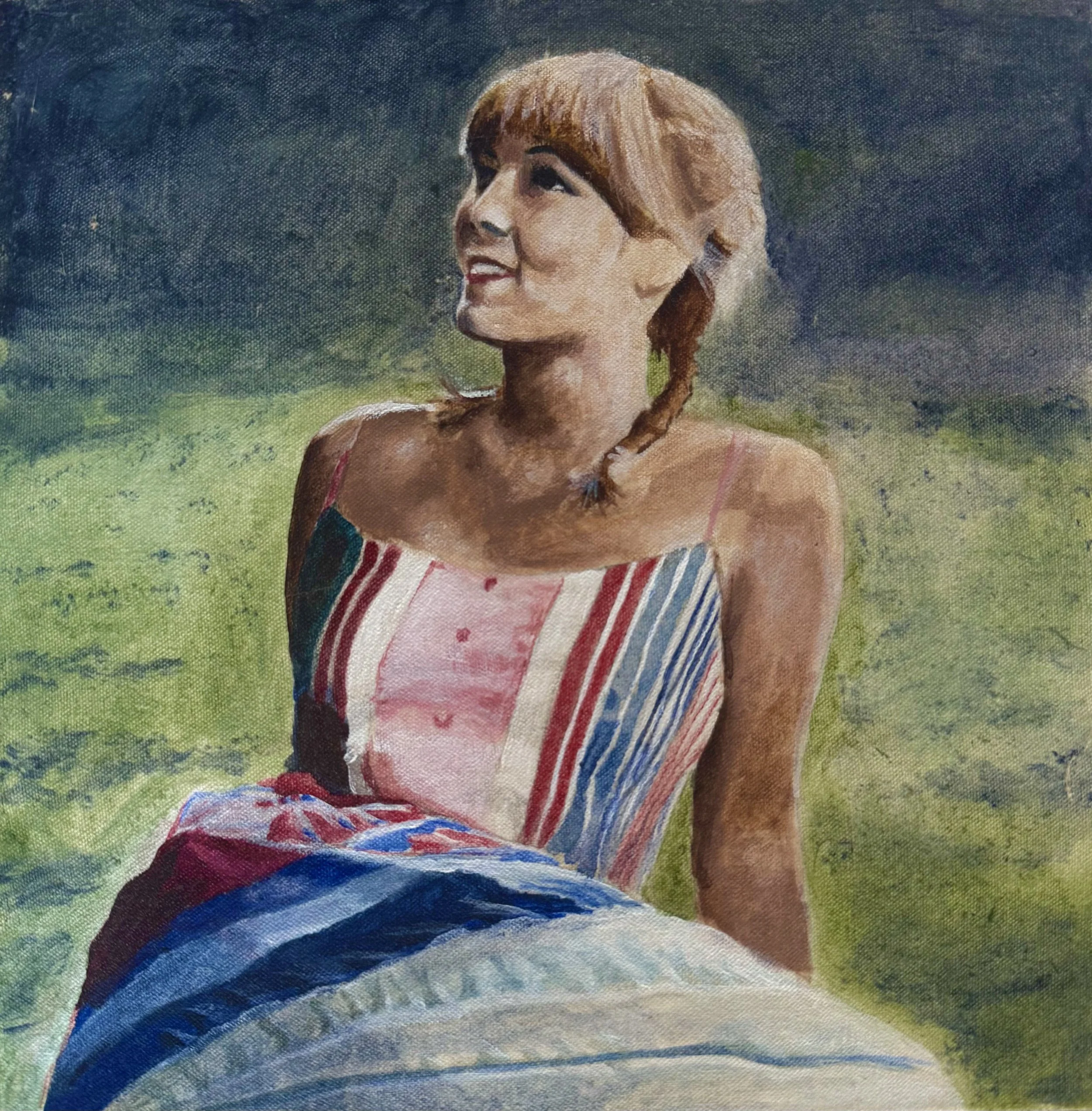 A woman with short brown hair and a braid, wearing a colorful striped dress, sitting outdoors on grass and looking up.