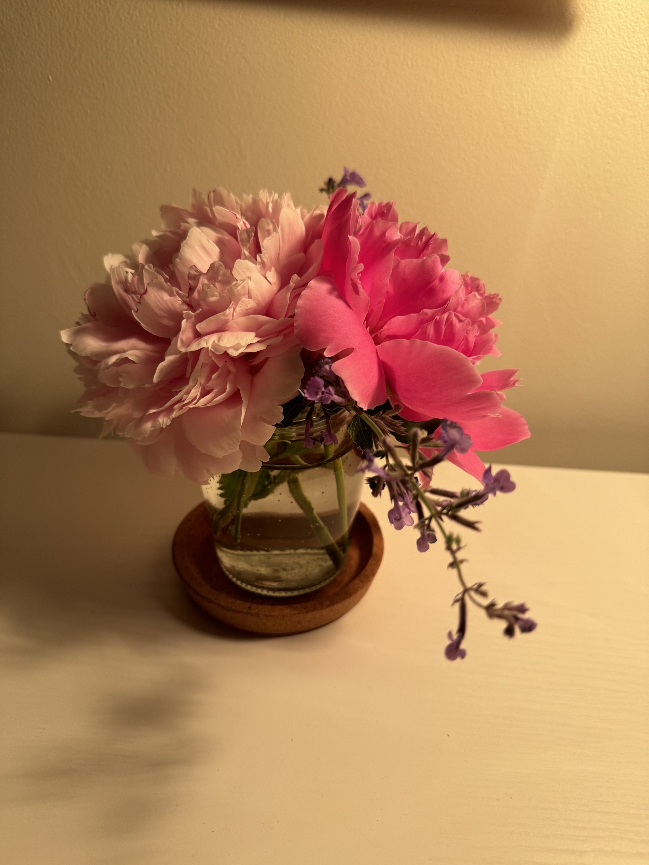 Pink and purple flowers in a glass vase on a wooden coaster