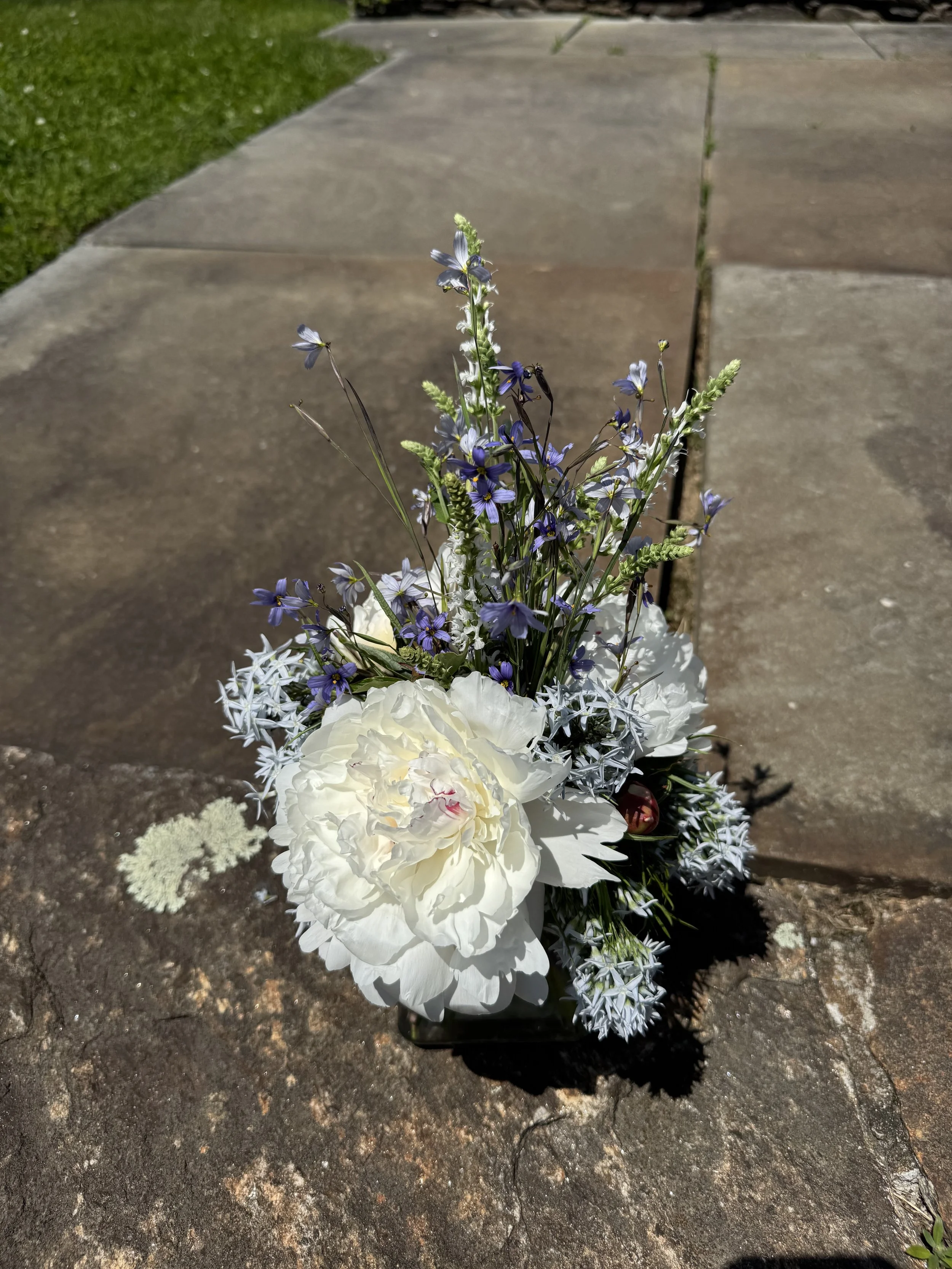 A small arrangement of white and purple flowers placed on a concrete sidewalk.