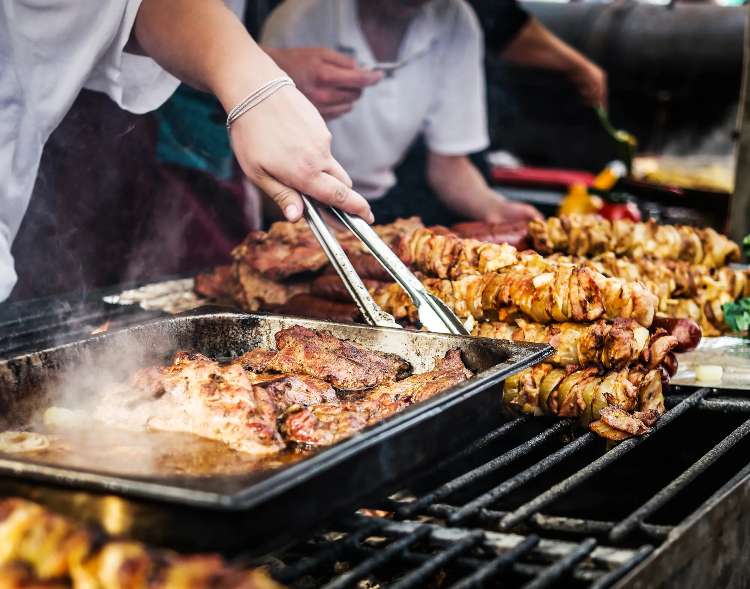 People grilling skewers of meat and chicken on a barbecue grill.