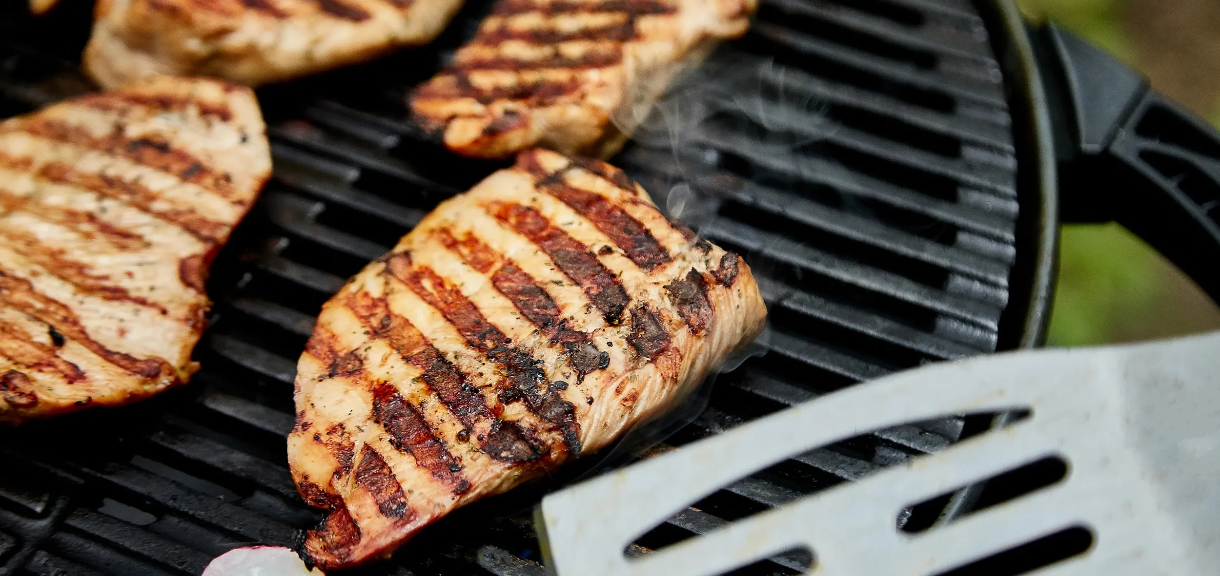 Grilled salmon fillets with grill marks cooking on a barbecue grill.