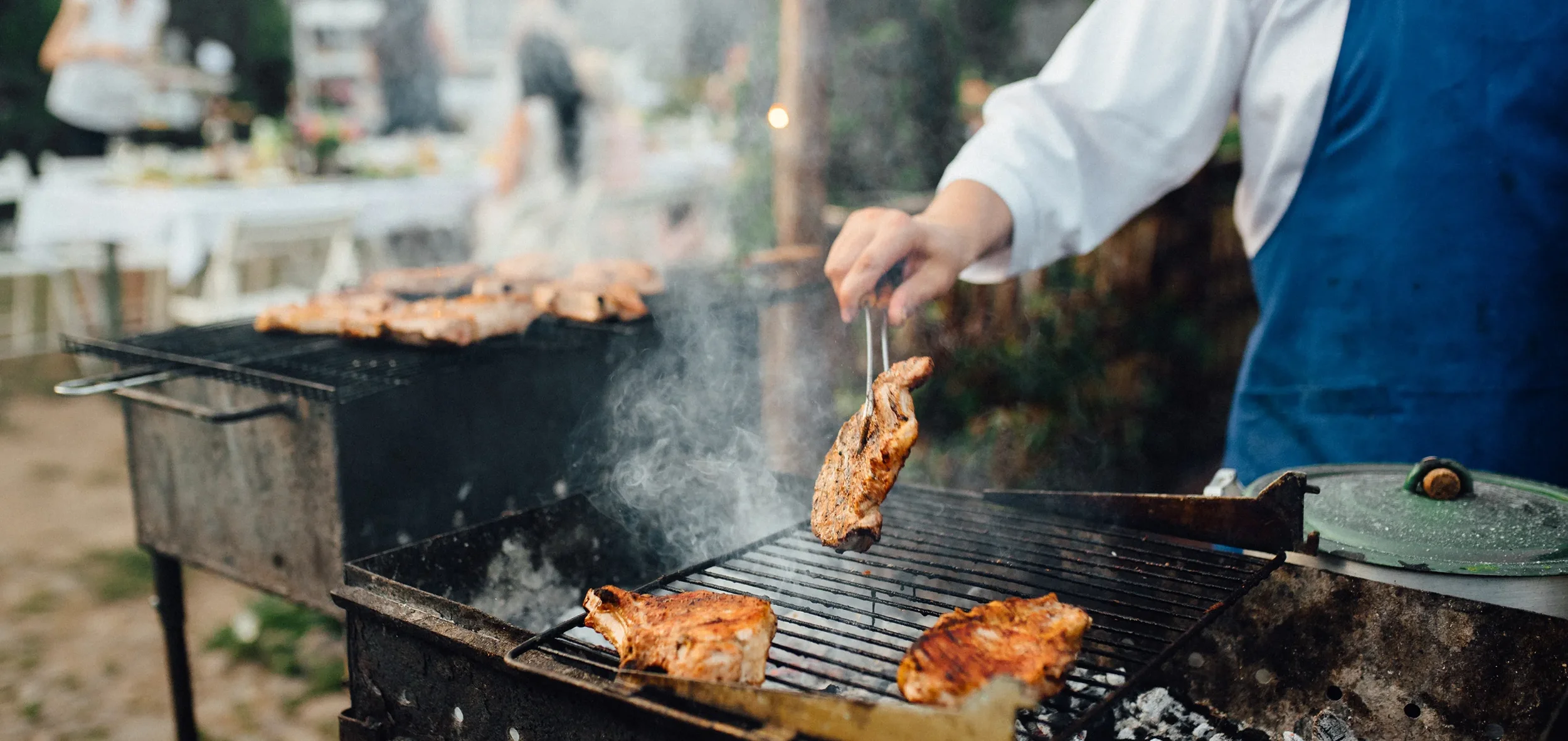Person grilling pork ribs and chicken on an outdoor barbecue grill
