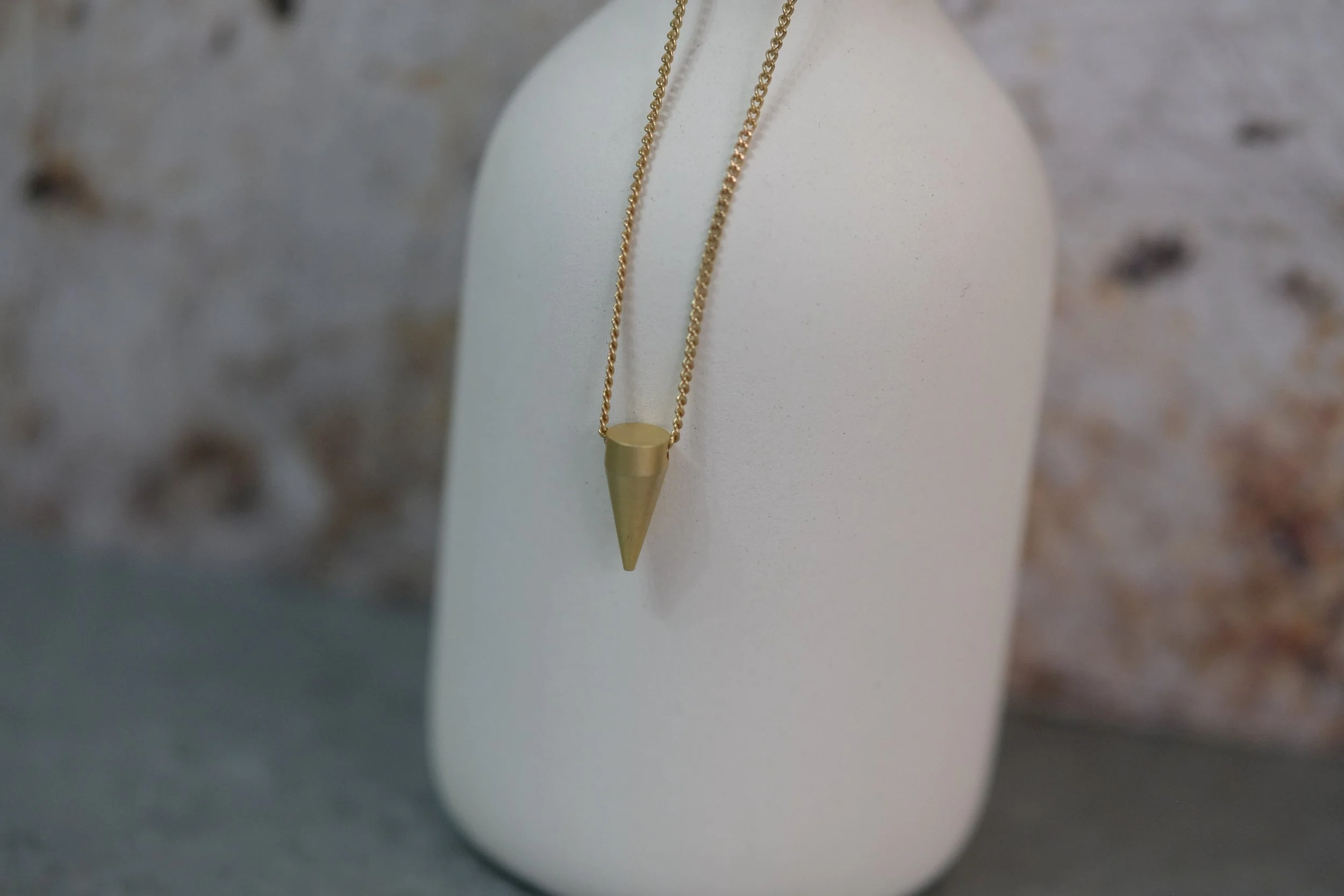 Gold necklace with a cone-shaped pendant displayed on a white stand.