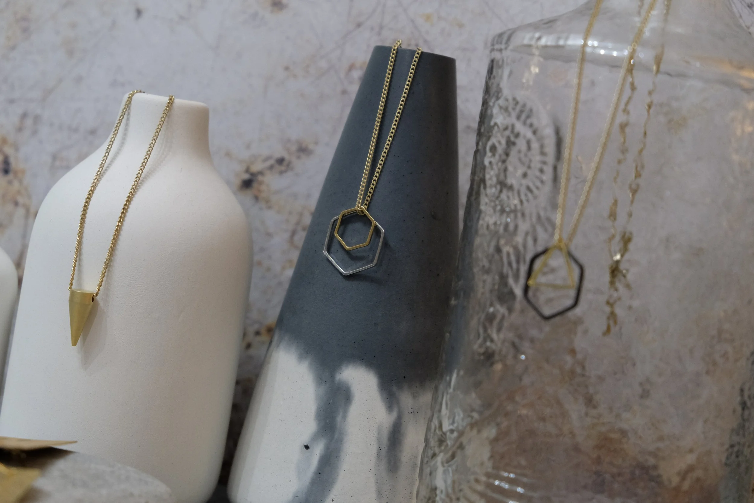 Necklaces with geometric pendants displayed on ceramic and glass busts and stands.
