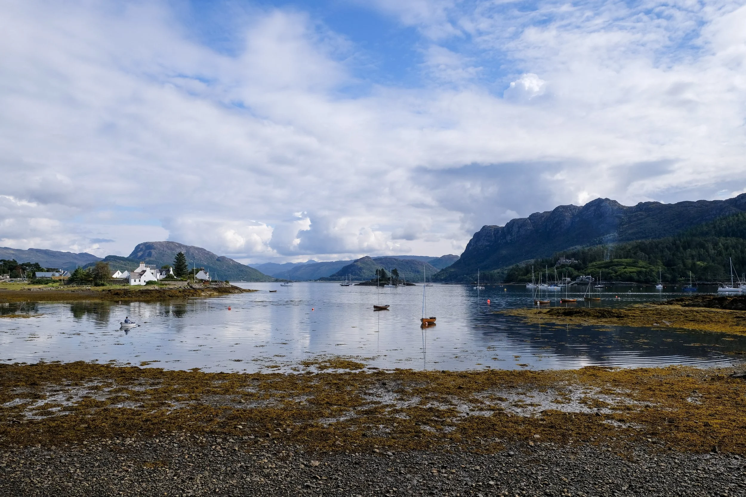 A scenic view of a calm lake with small boats floating, surrounded by mountains and a partly cloudy sky.