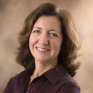 A woman with shoulder-length brown hair smiling, wearing a dark purple shirt.