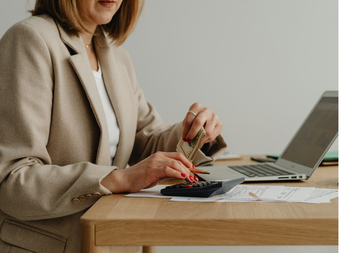 Woman doing bookkeeping at a desk with a calculator, papers, and a laptop.