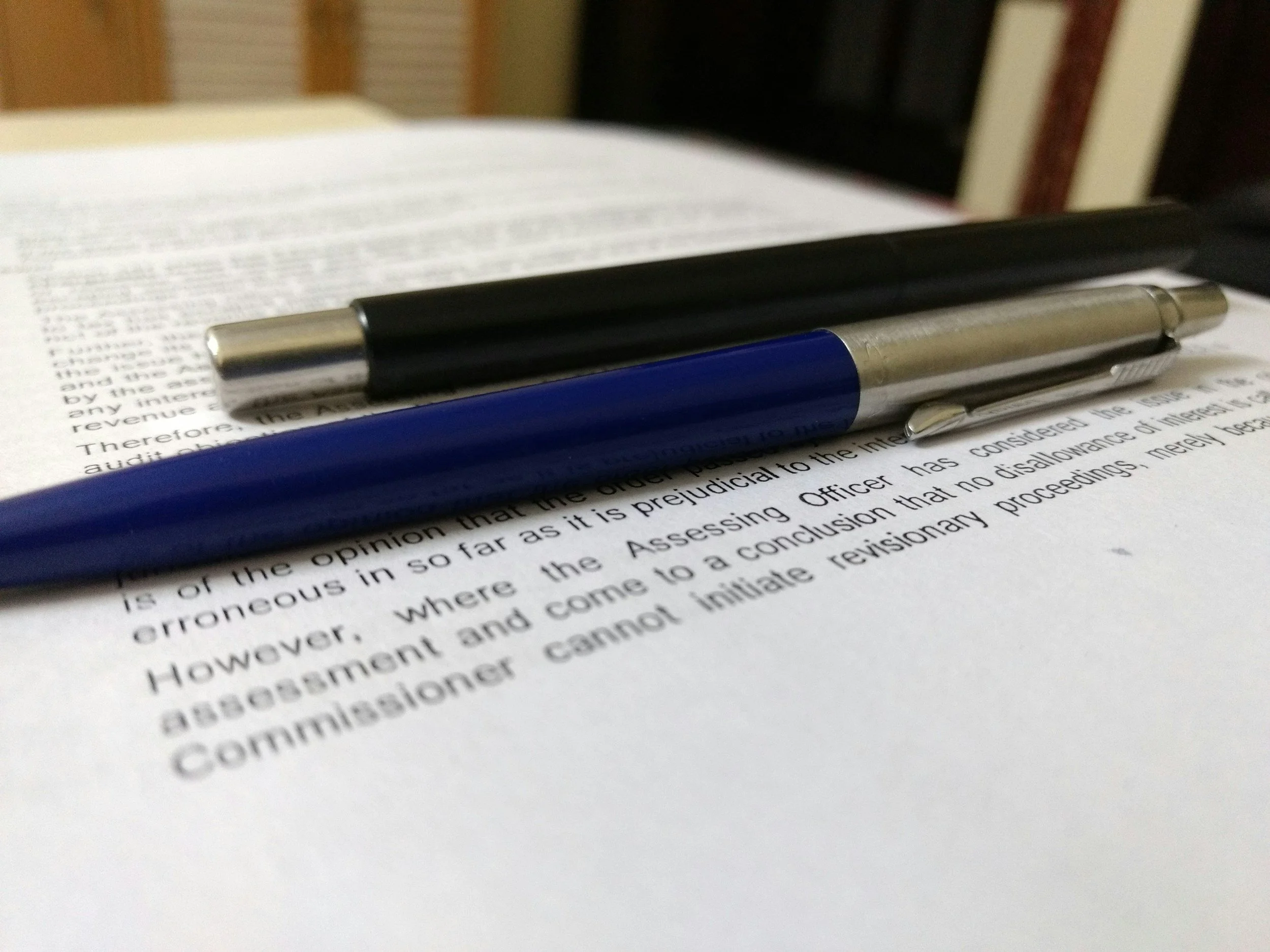 Close-up of two pens resting on an open legal or official document on a desk.