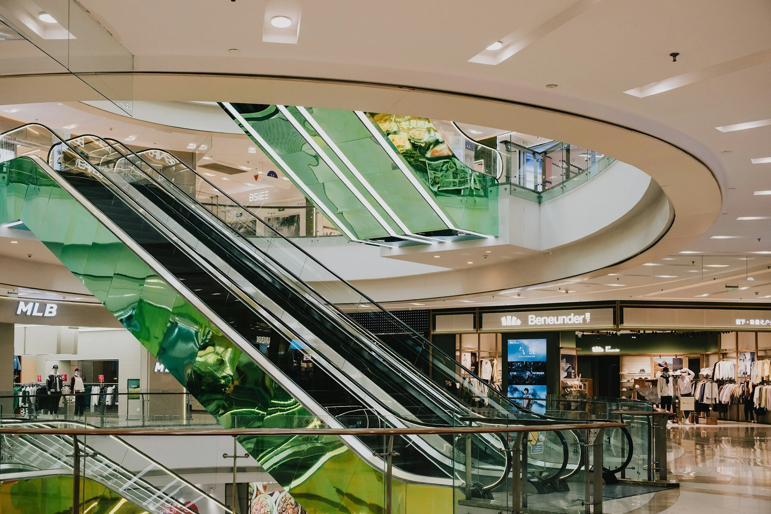 Interior of a shopping mall with multiple escalators, storefronts, and people shopping.