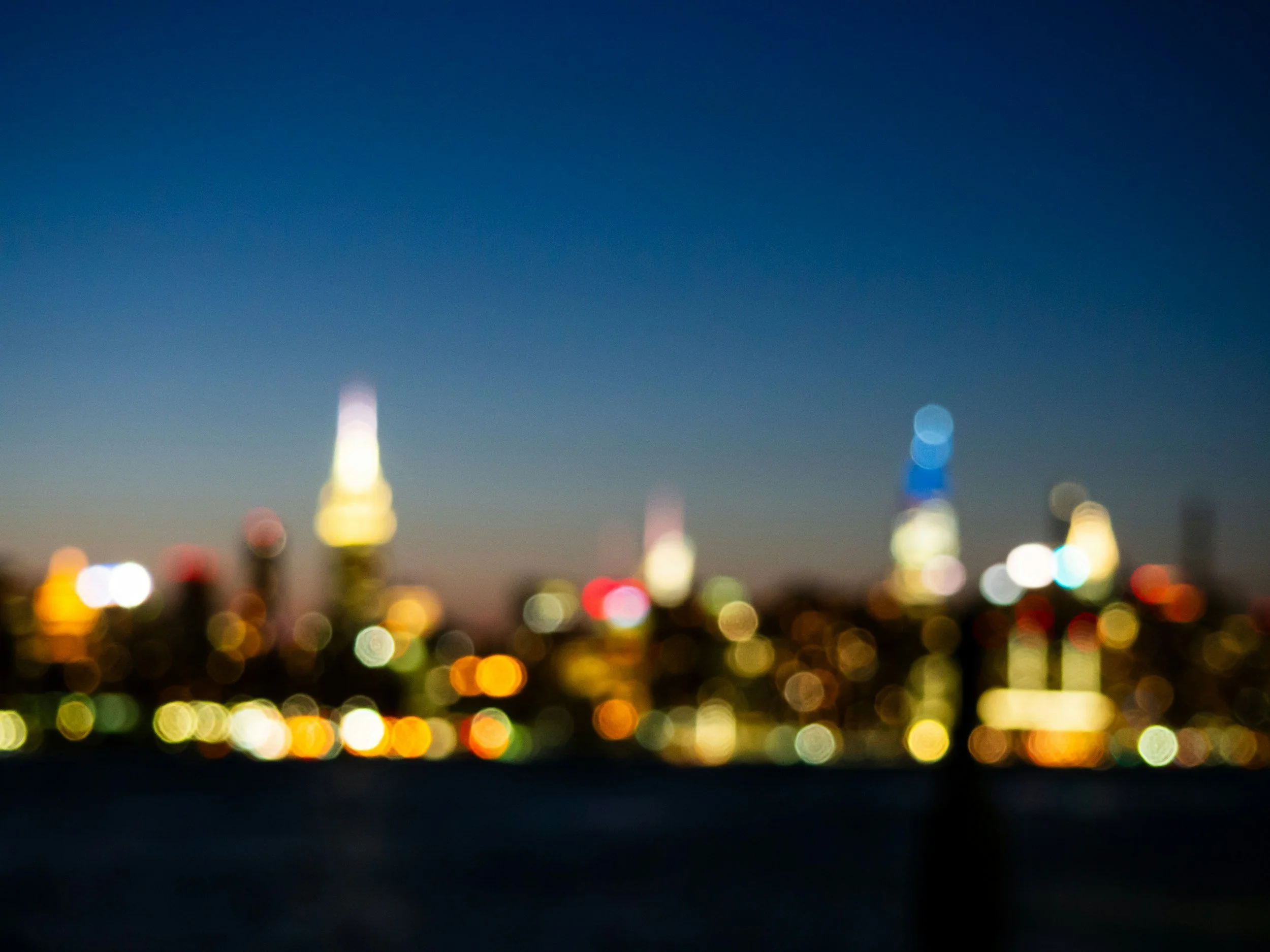 Blurred city skyline at night with colorful lights and a dark blue sky.