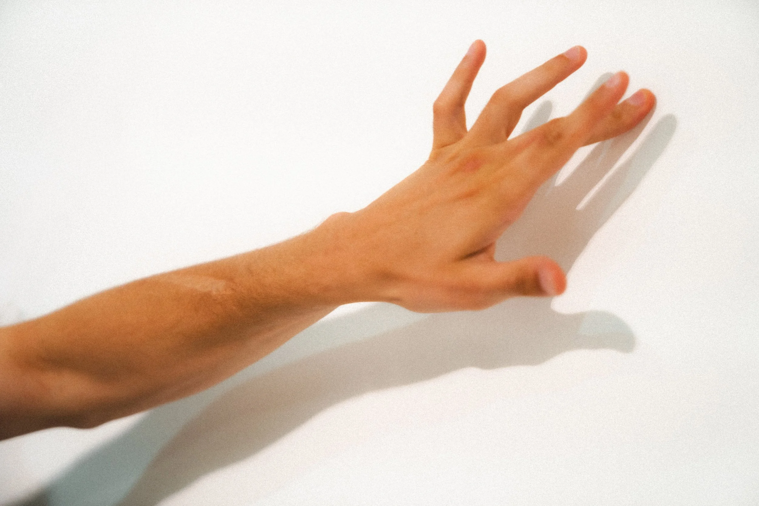 A human hand with fingers slightly spread, casting a shadow on a white surface.