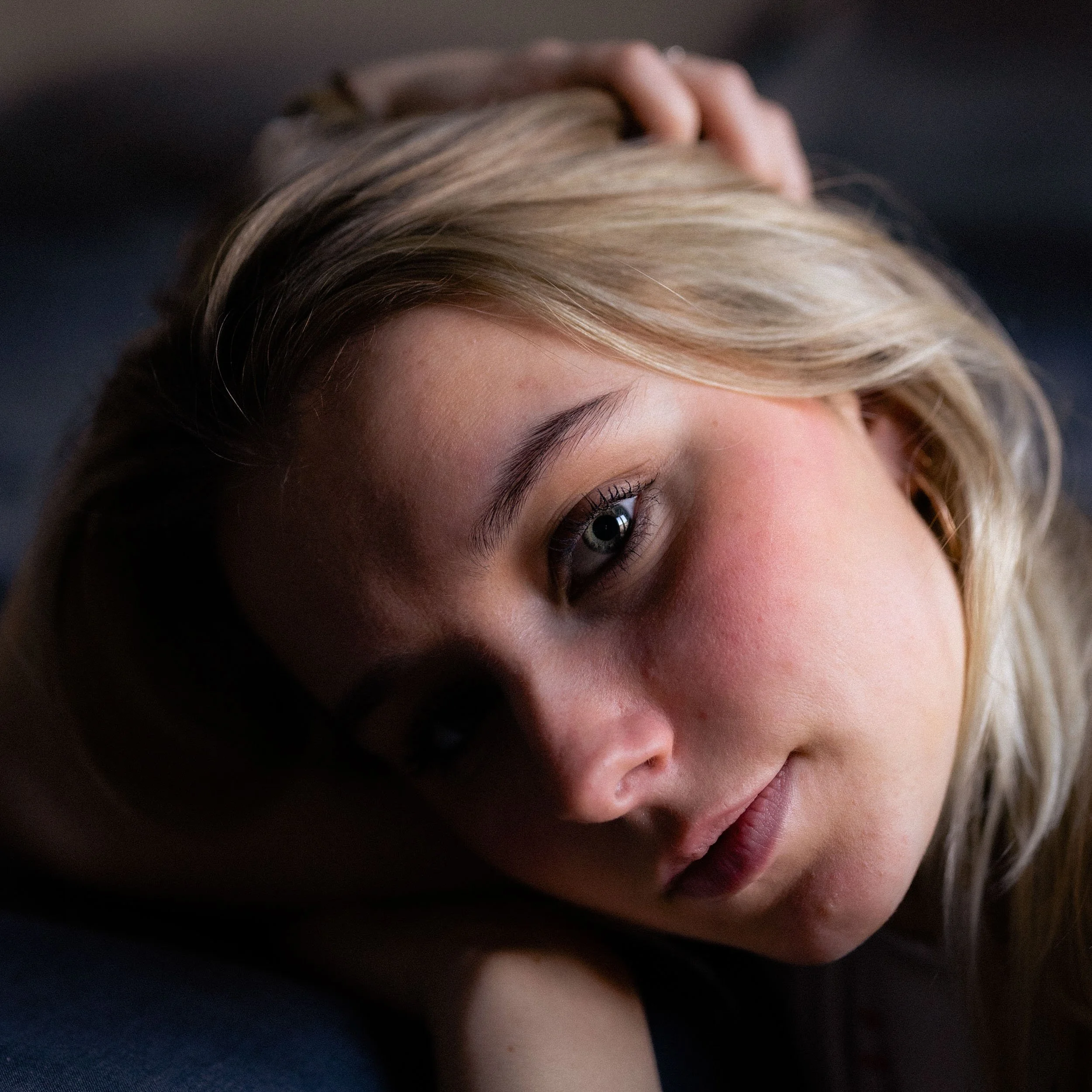 Close-up of a young woman with blonde hair lying down, looking at the camera with a calm expression.