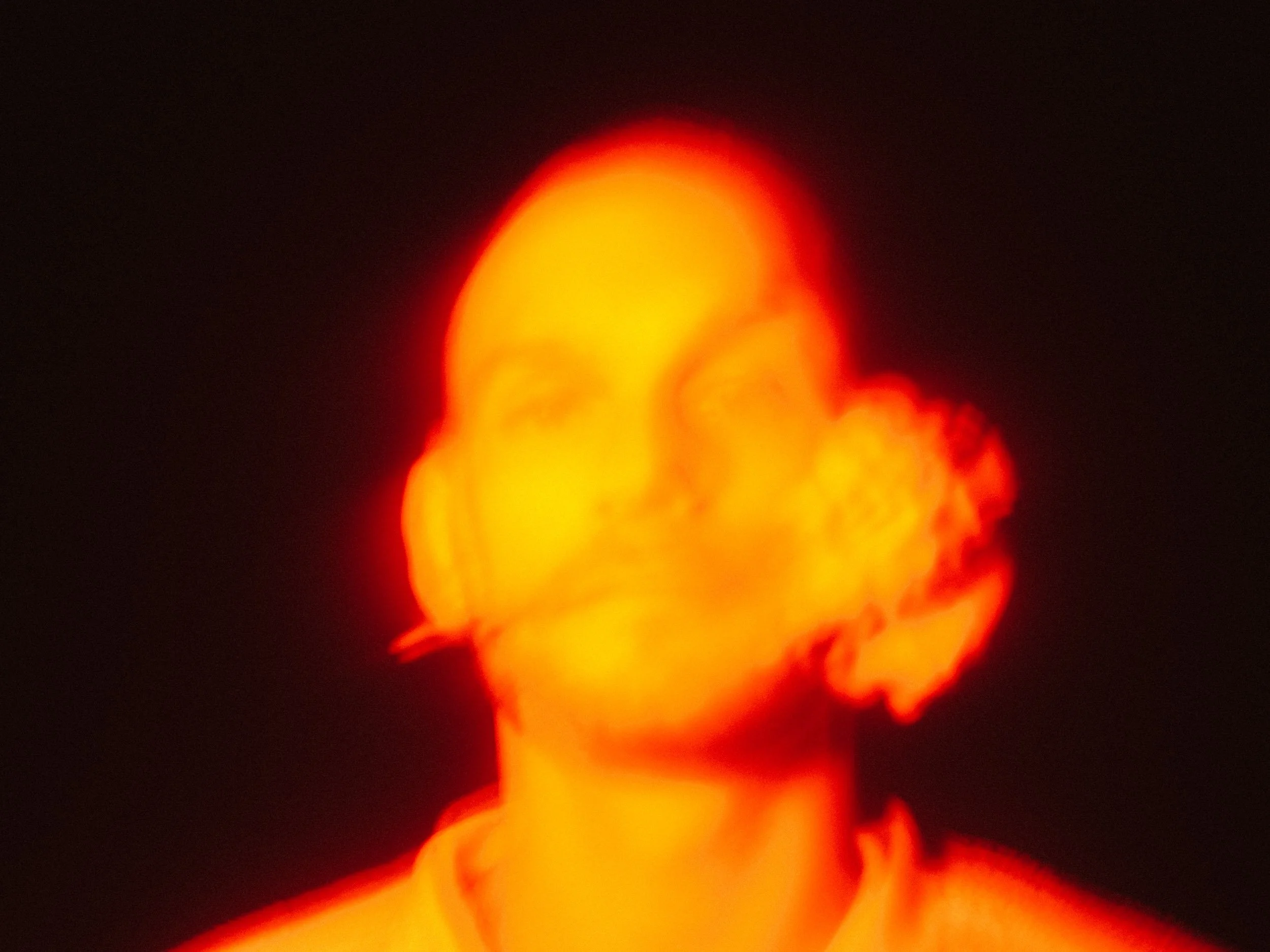 A glowing, blurred image of a person with short hair against a dark background, illuminated in warm orange and red tones.