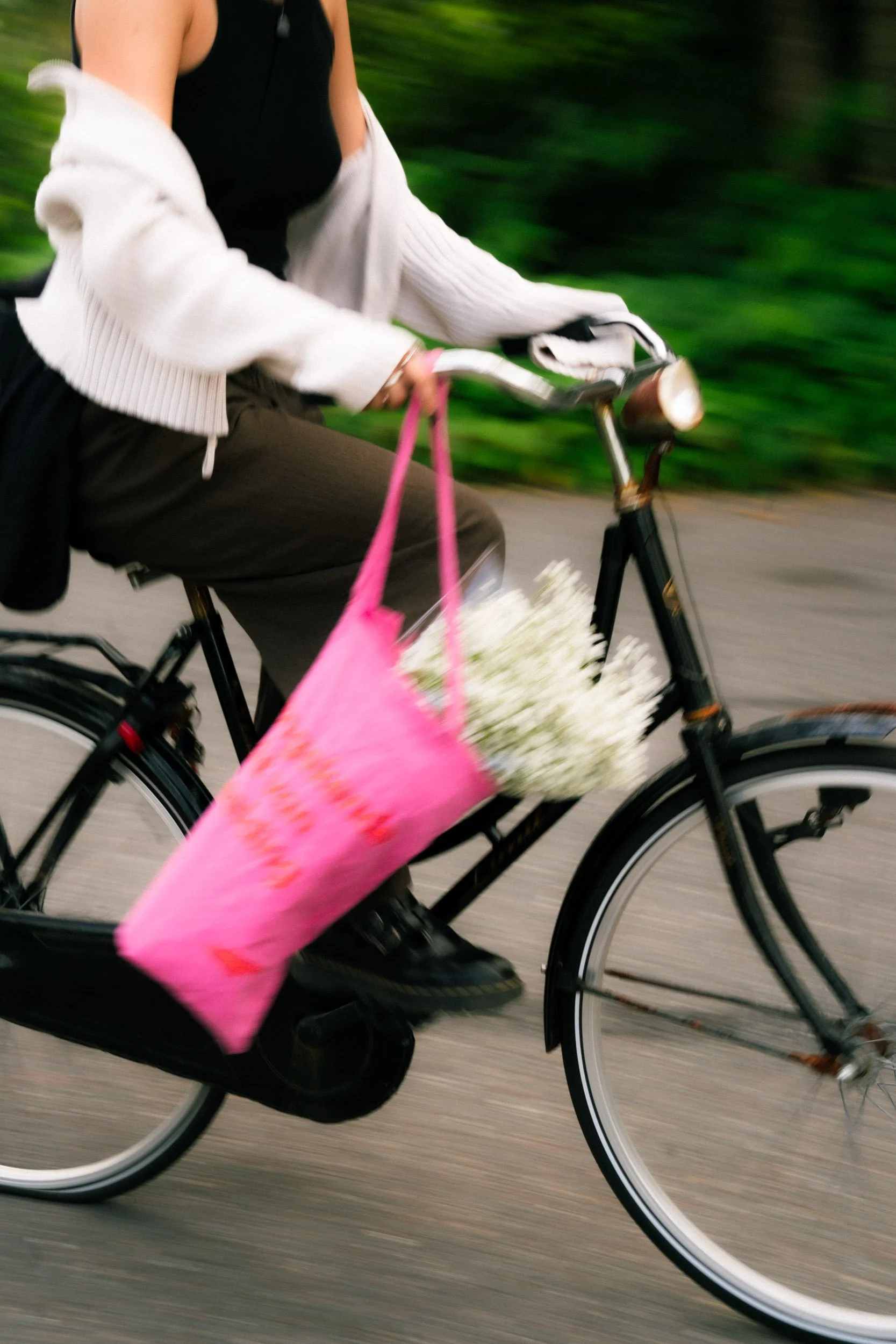 Person riding a bicycle with a pink bag filled with white flowers attached to the front.