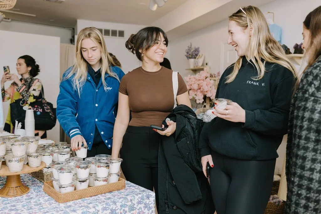 Group of women at a dessert table, serving and chatting at a social event.