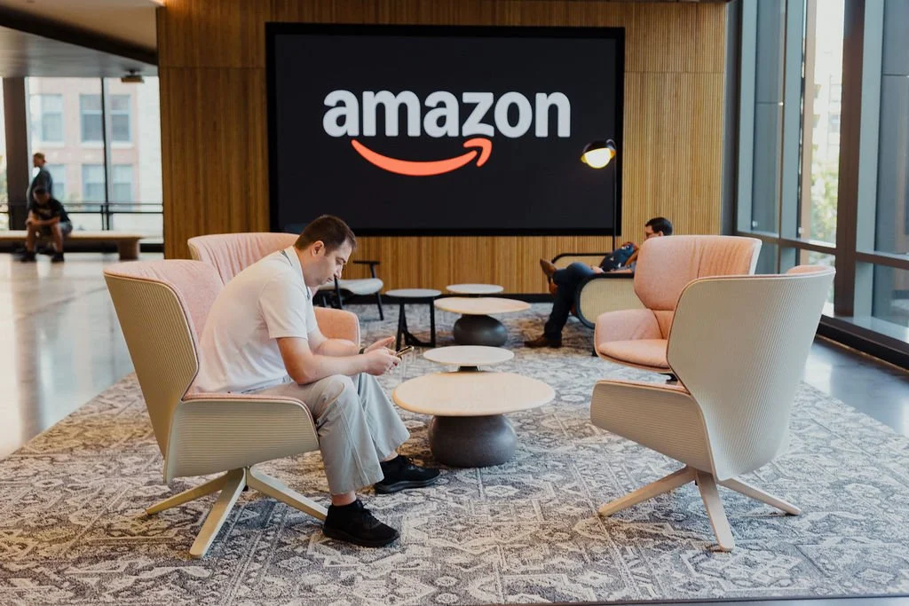 Lobby seating area with four people, large Amazon sign on the wall, modern furniture and large windows.