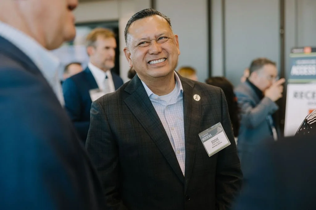 A man smiling at a professional event, wearing a dark blazer and a name tag that says Eddie.