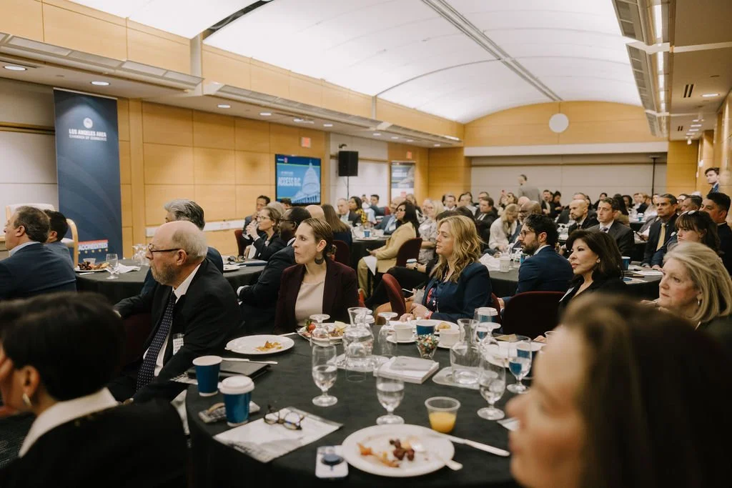 Business conference with attendees seated at tables, listening to a speaker or presentation.
