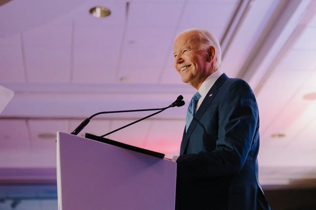 Joe Biden smiling while speaking at a podium during a formal event.
