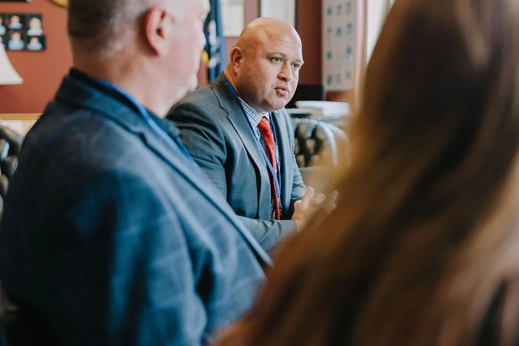 A man in a suit having a serious conversation with two other people in a professional office setting.