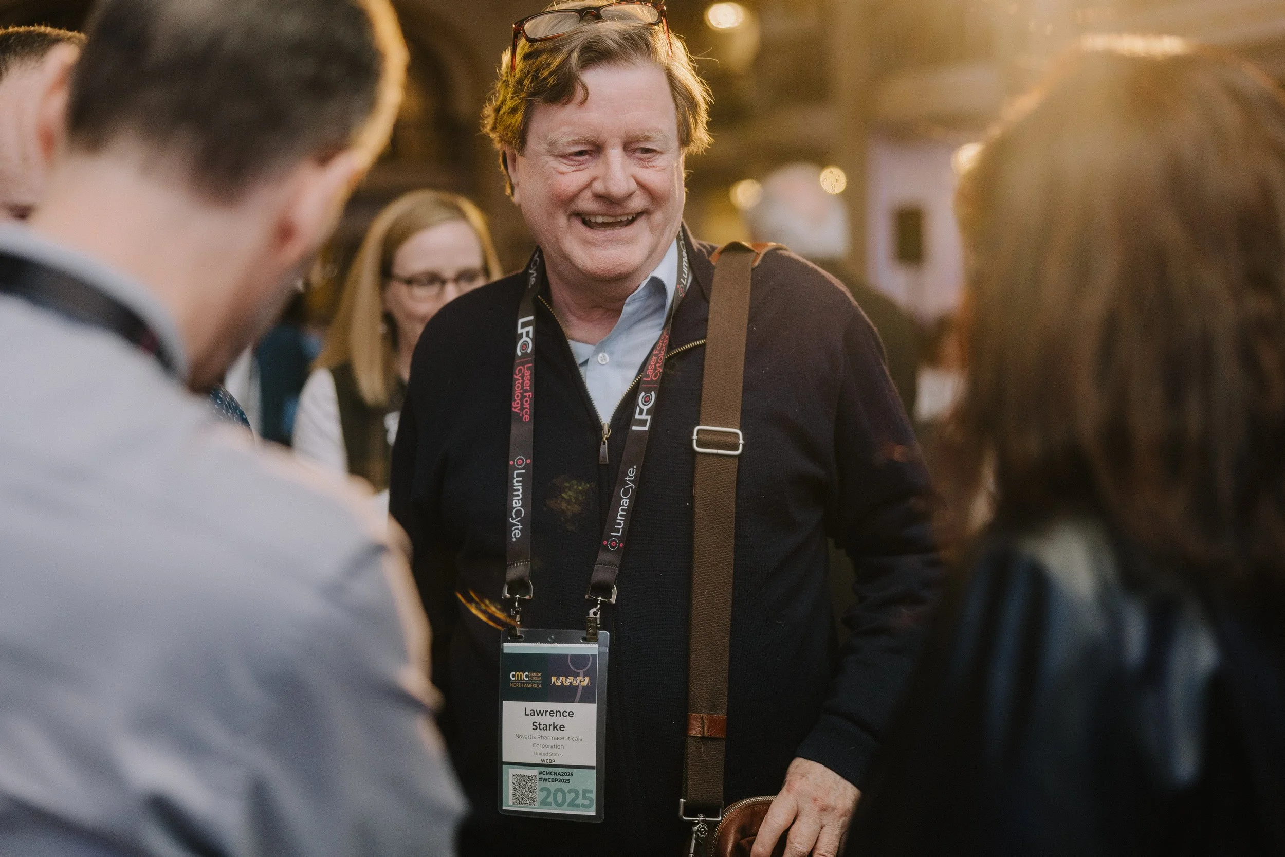 Man wearing a conference badge and lanyard, smiling and talking to people at a professional event.