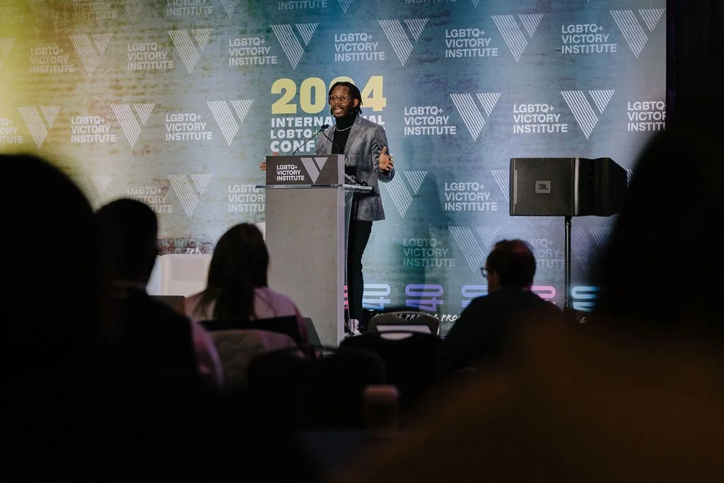 A man speaking at a podium on a stage during the LGBTQ+ Victory Institute 2024 International Conference, with audience members visible in the foreground.