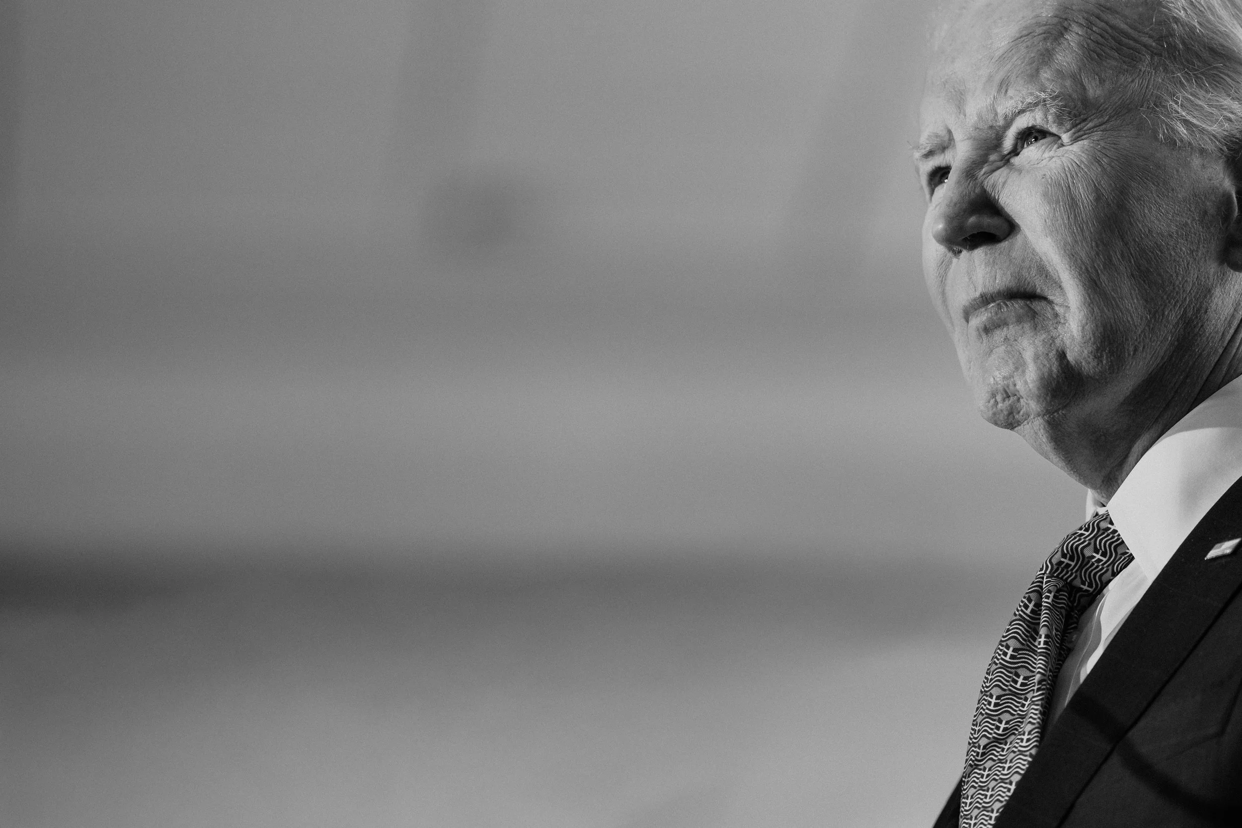 A black and white close-up photograph of an elderly man in a suit, looking to his left with a serious expression.