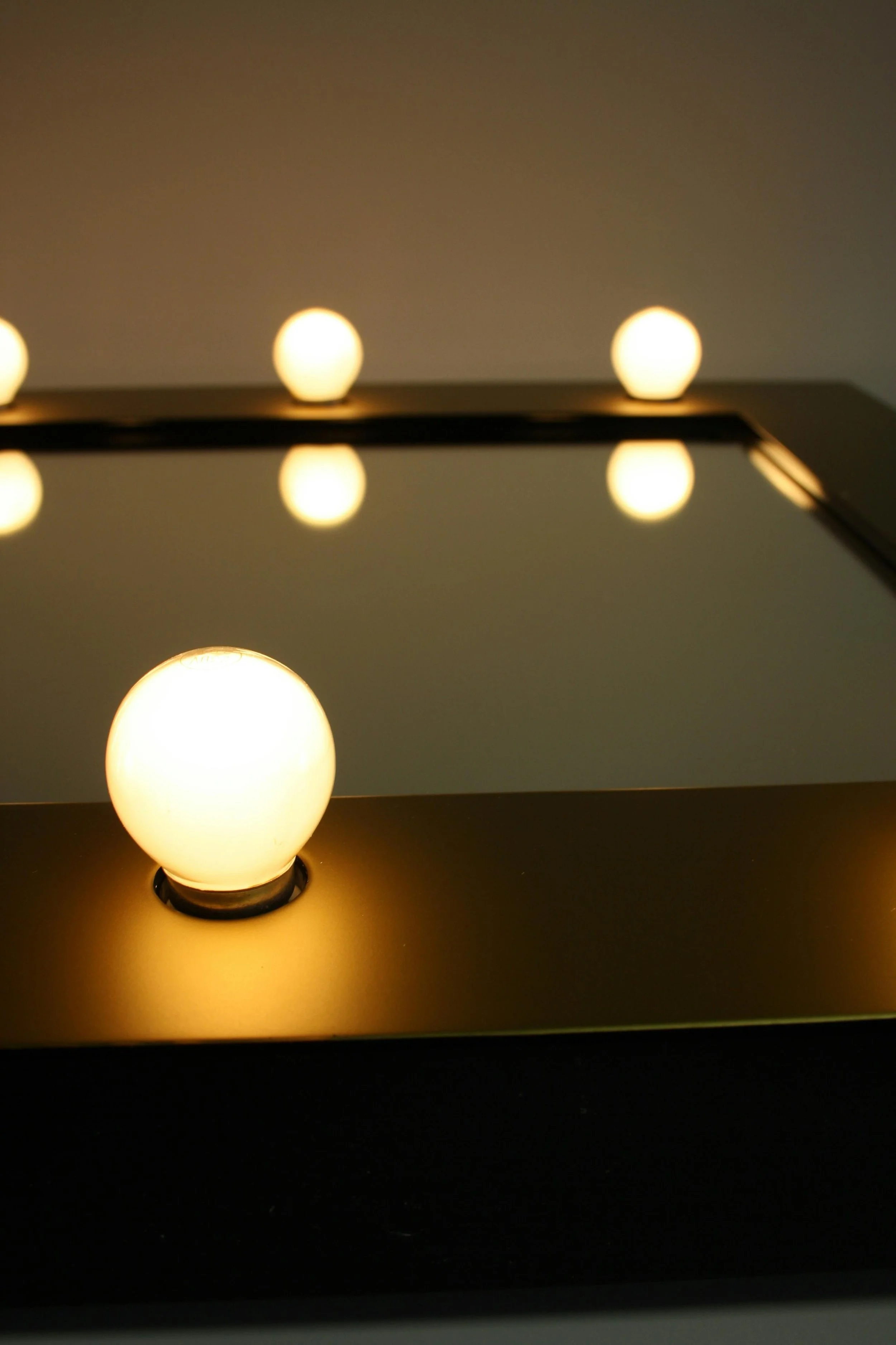 Close-up of a modern light fixture with a row of glowing spherical bulbs reflected on a mirror surface.