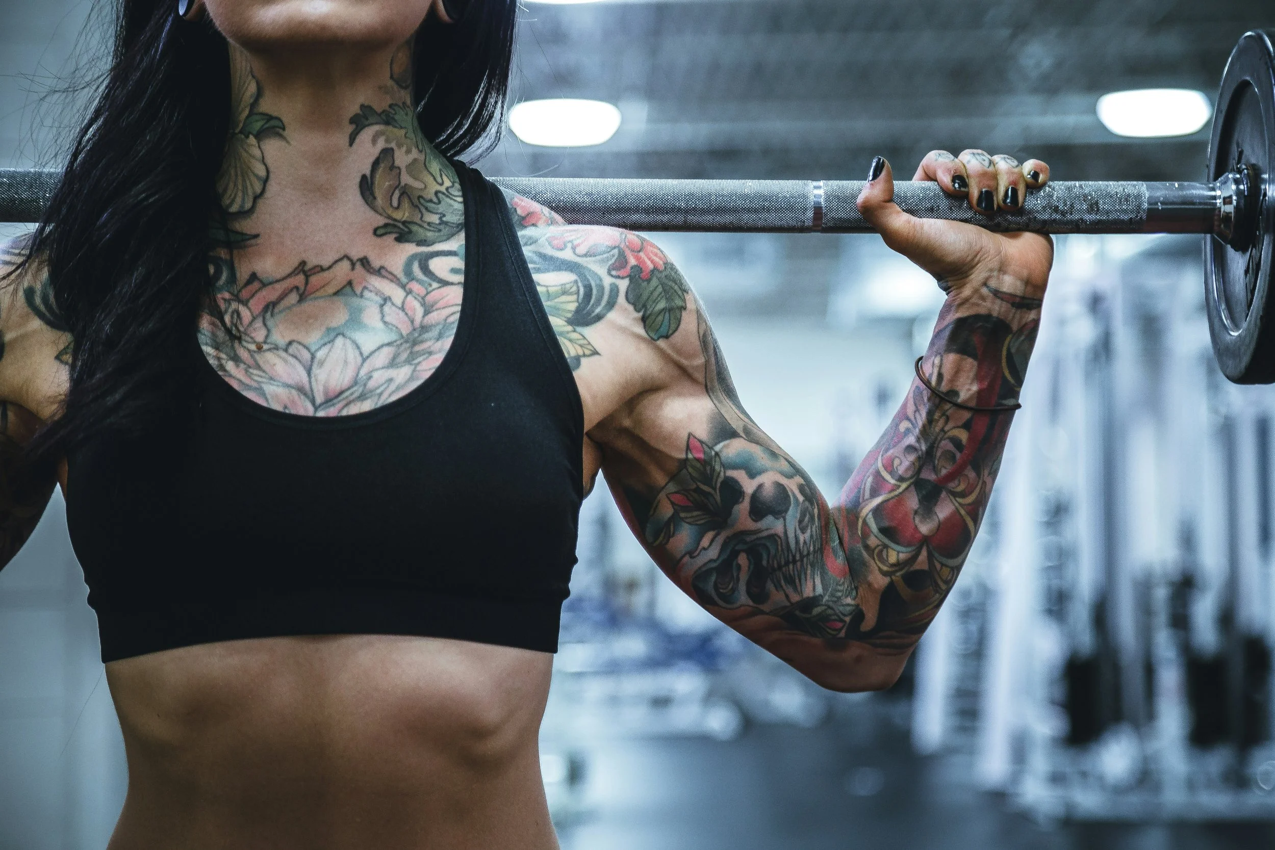 A woman with tattoos lifting a barbell in a gym.