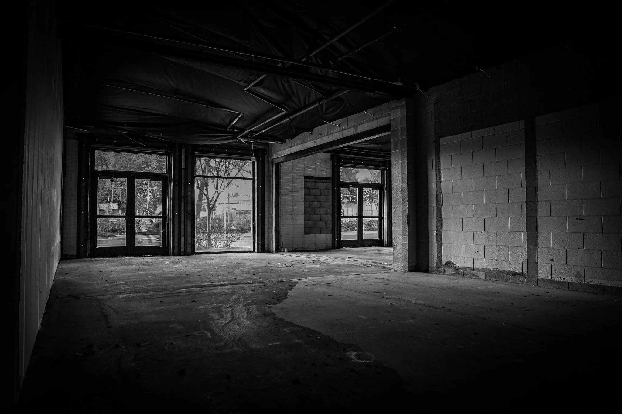 Interior of an under-construction building with exposed walls, ceiling, and large windows showing trees outside.