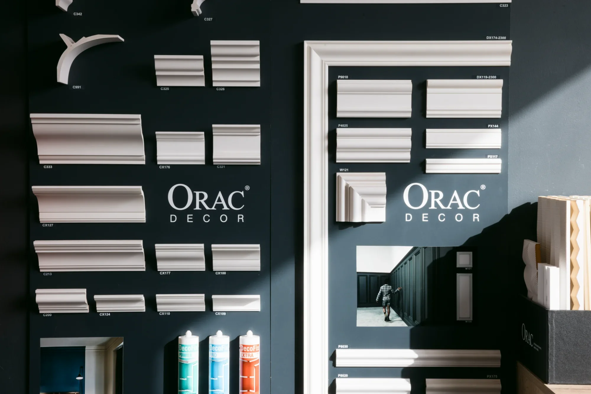Exposition de moulures décoratives blanches sur un panneau noir avec le logo 'ORAC DECOR'