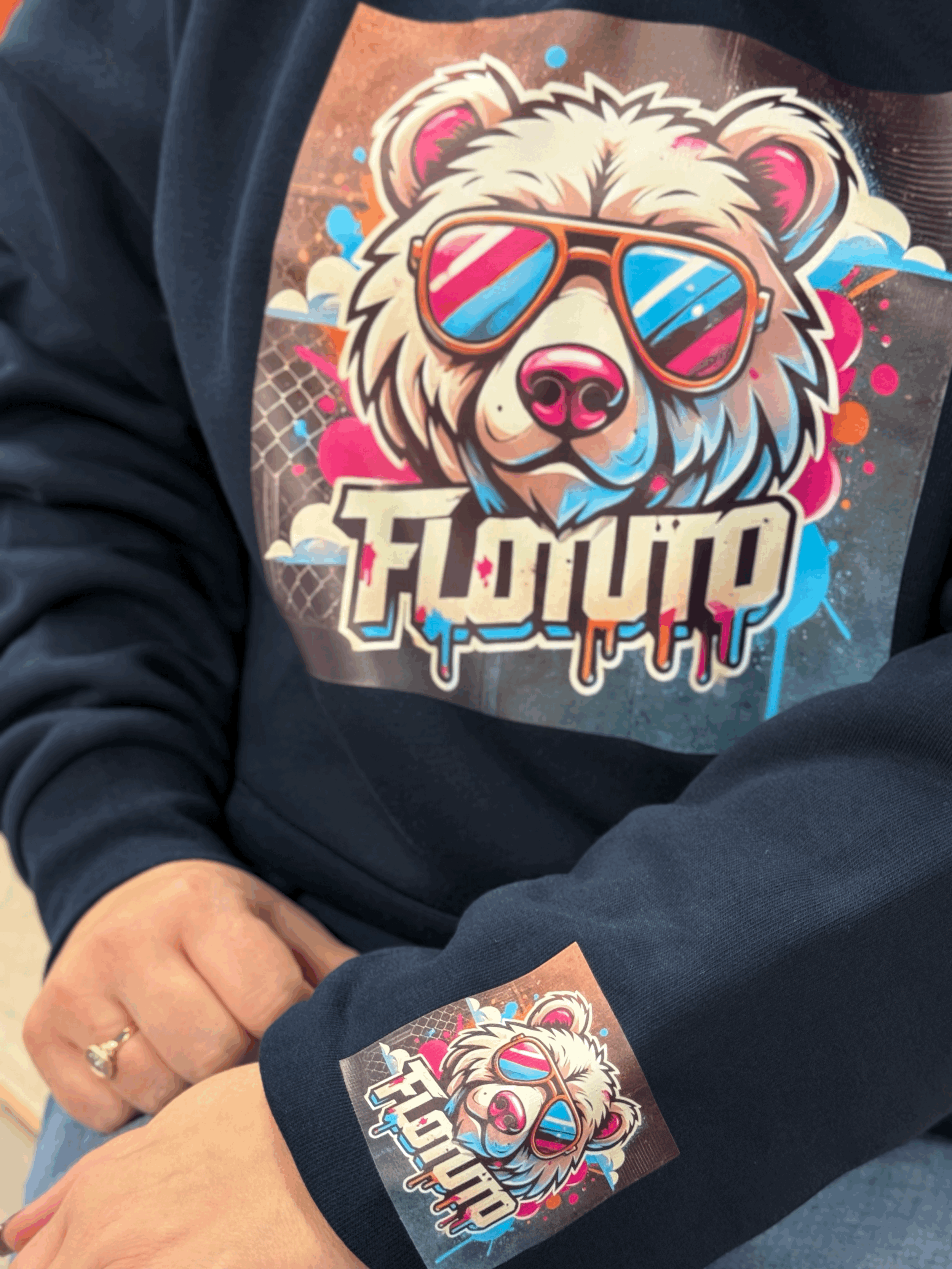 Une personne portant un sweat-shirt noir avec un logo coloré représentant un ours portant des lunettes de soleil. Le logo comporte le texte 'LION' en dessous.