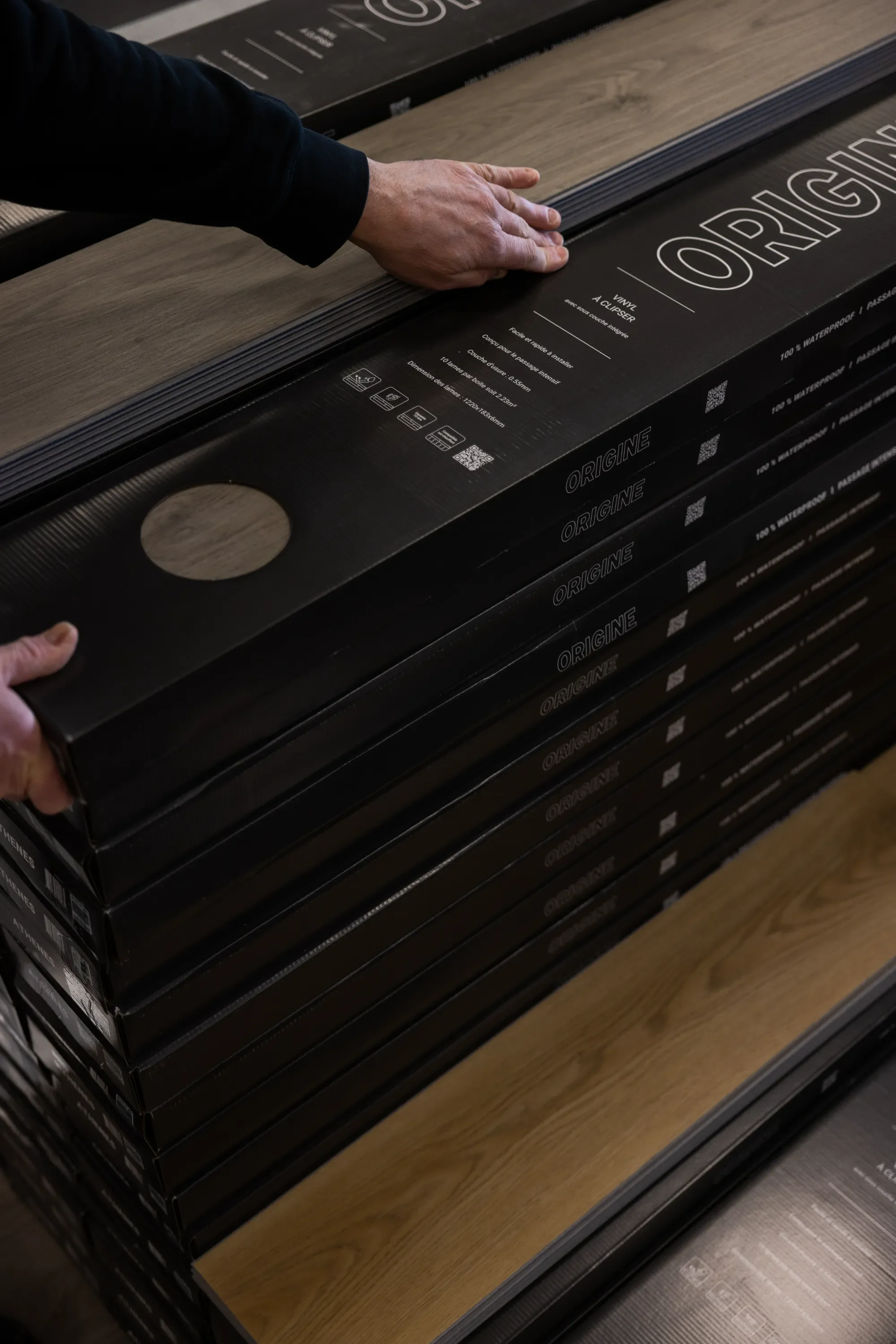 Main d'une personne manipulant une planche de bois dans un magasin de matériaux ou de décoration intérieure.